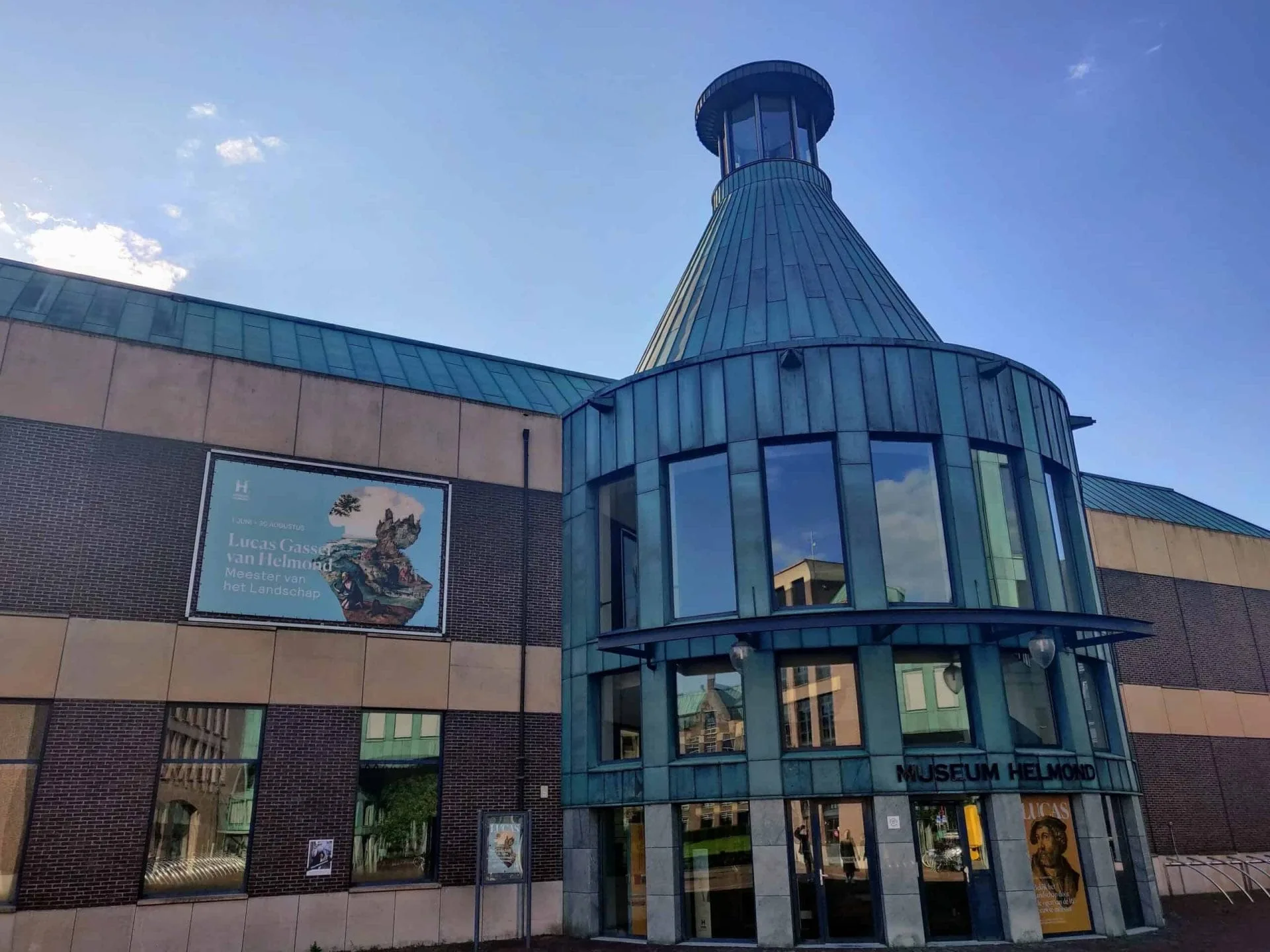 Exterieur van Museum Helmond met een opvallende ronde toren van groen koper en een poster van de Lucas Gassel-expositie