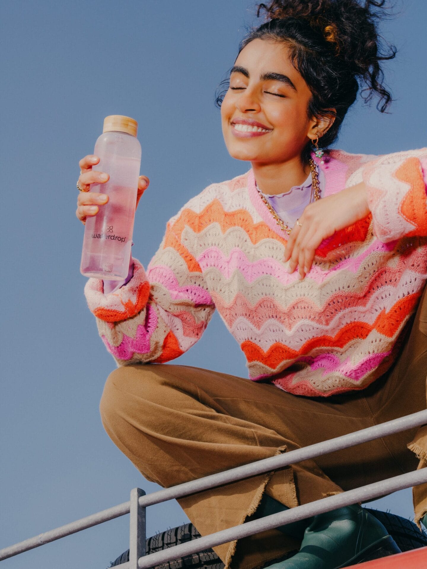 Een lachende jonge vrouw met een Waterdrop-fles gevuld met een roze drankje