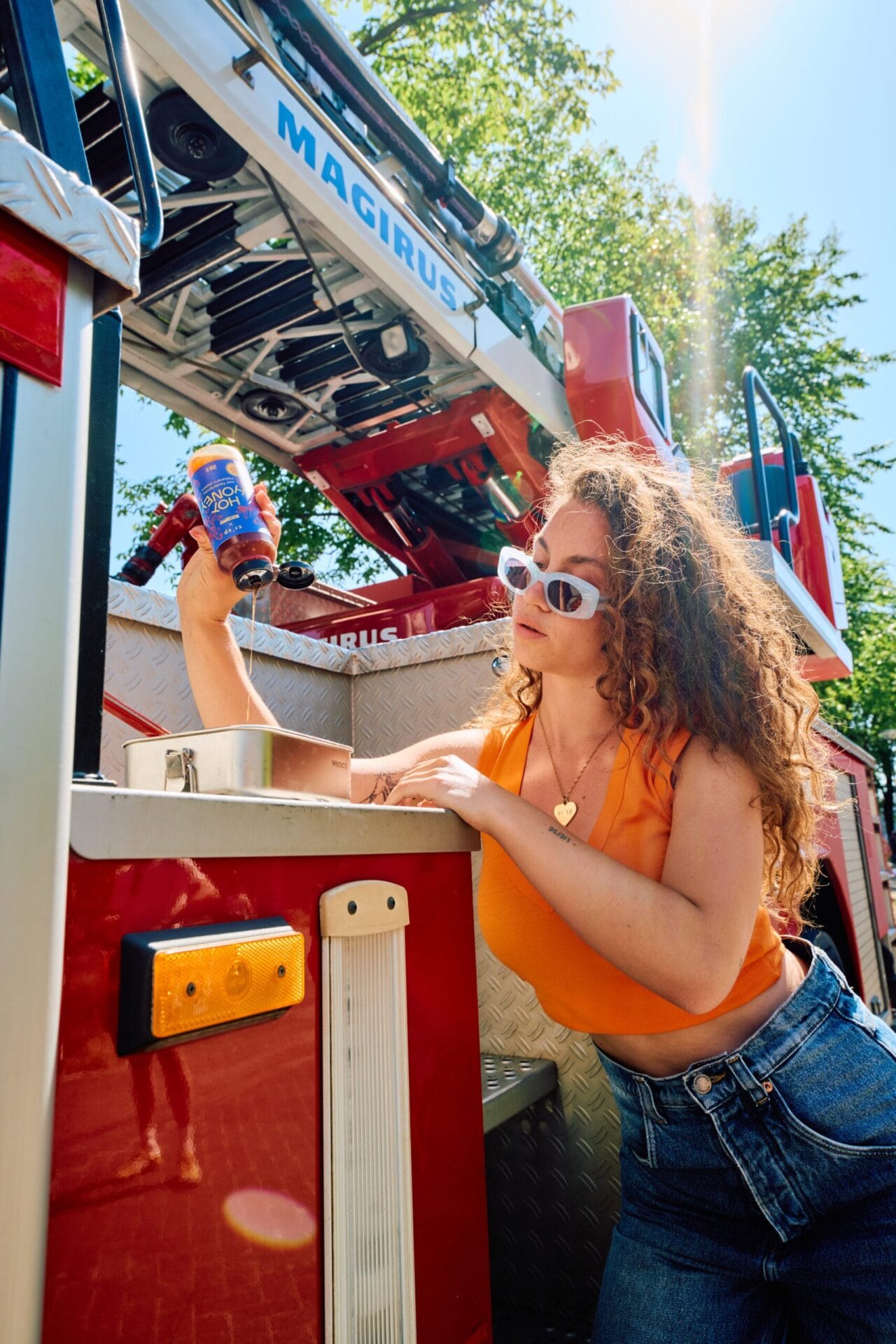 Een vrouw giet Crisp Hot Honey uit een flesje over eten, staand voor een brandweerauto
