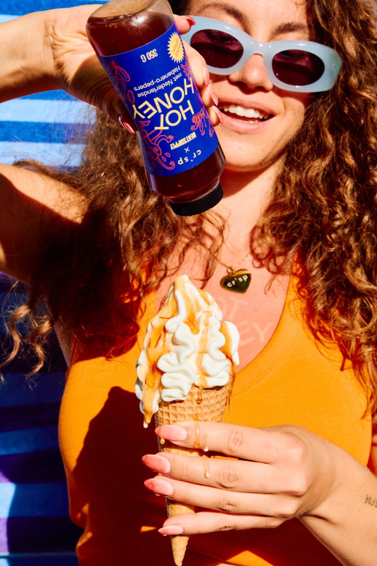 Een lachende vrouw giet Crisp x Heatsupply Hot Honey over een softijsje in een hoorntje