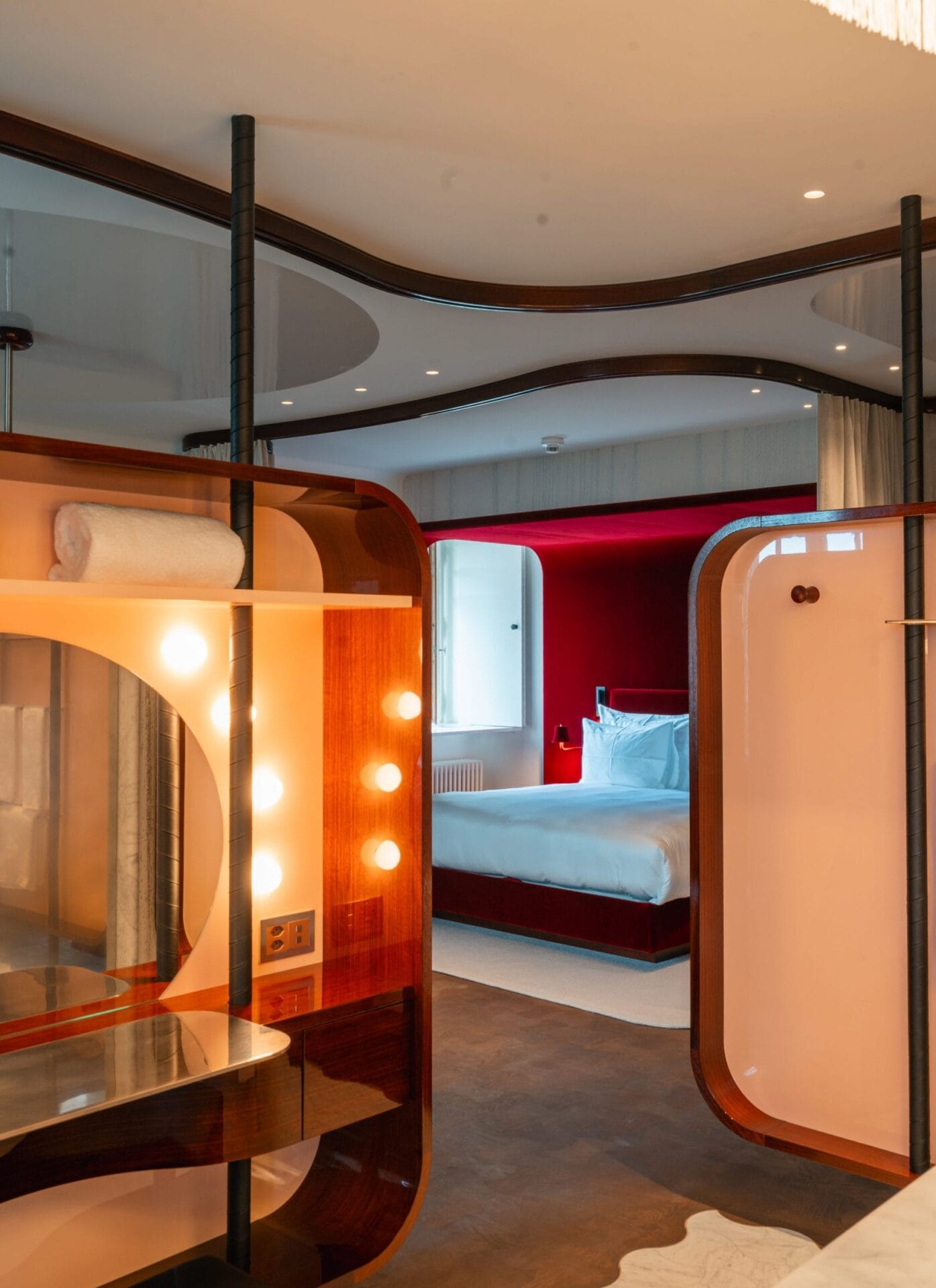 Interieur van een suite met mahoniekleurige kasten, een verlichte spiegel en een bed in een nis van rood velours