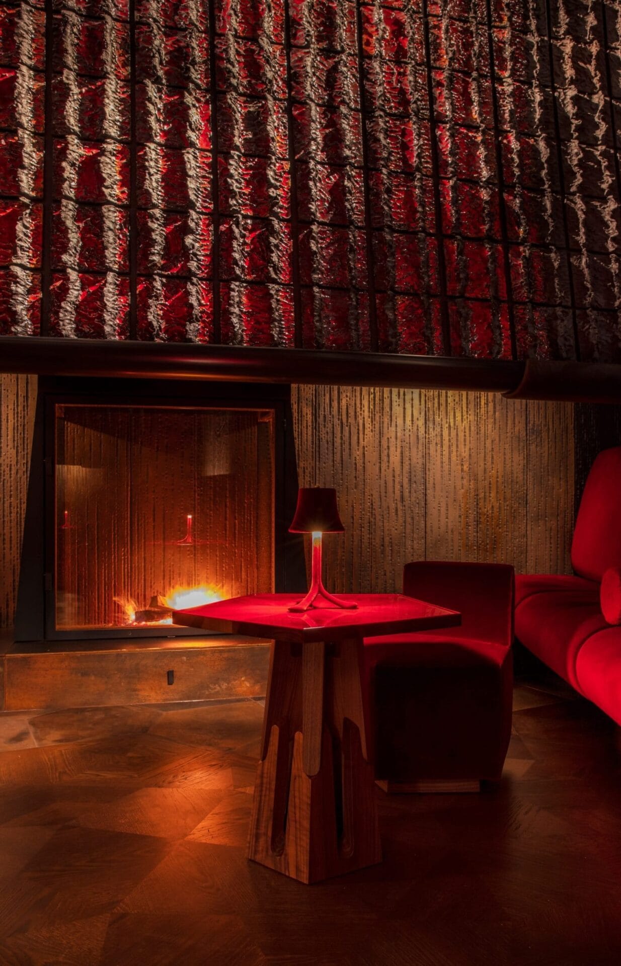 Interieur van de rokerslounge met een brandende open haard, rood velours meubilair en een houten tafel met lampje