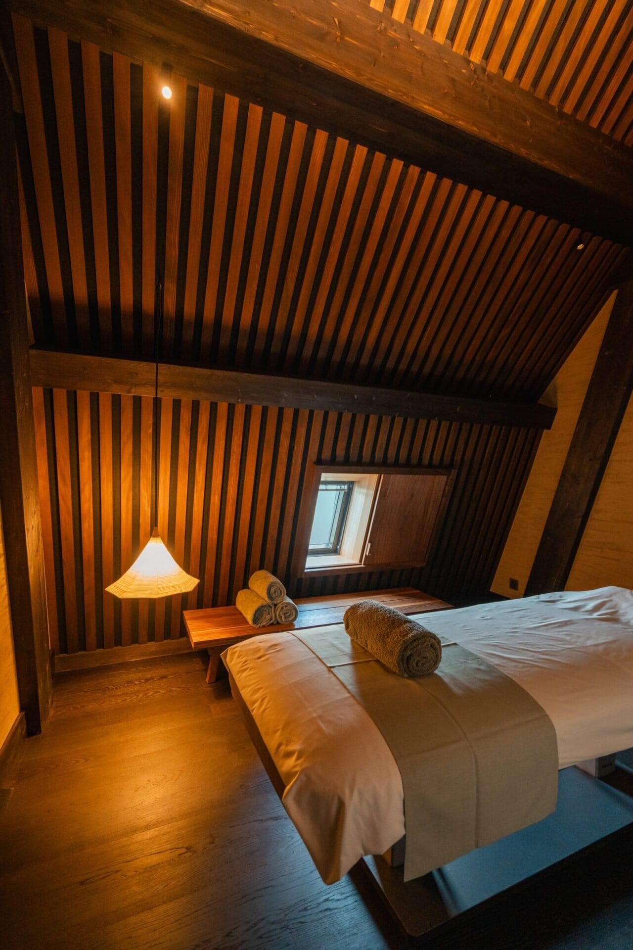 Minimalistische spa-ruimte in Japanse onsen-stijl met houten lattenwanden, een massagetafel en sfeervolle verlichting