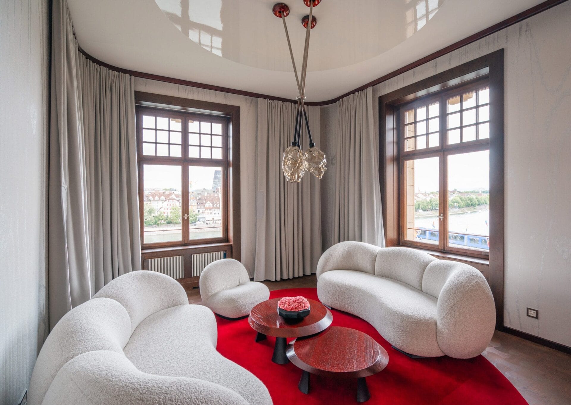 Modern interieur van een suite met witte organisch gevormde banken op een rood tapijt en uitzicht op de Rijn