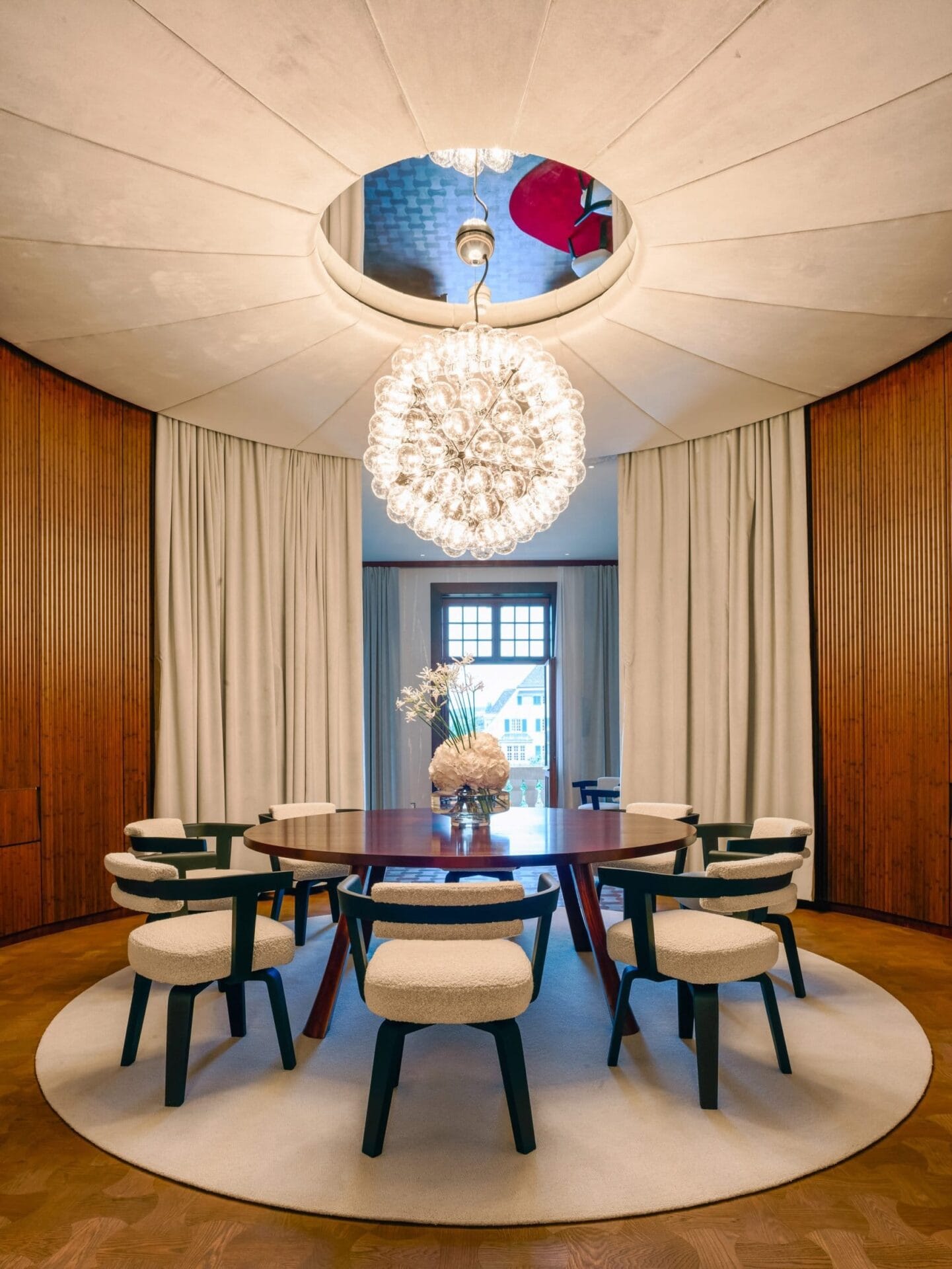 Interieur van een suite in Hotel Les Trois Rois met een ronde houten tafel, moderne stoelen en een bolvormige lamp