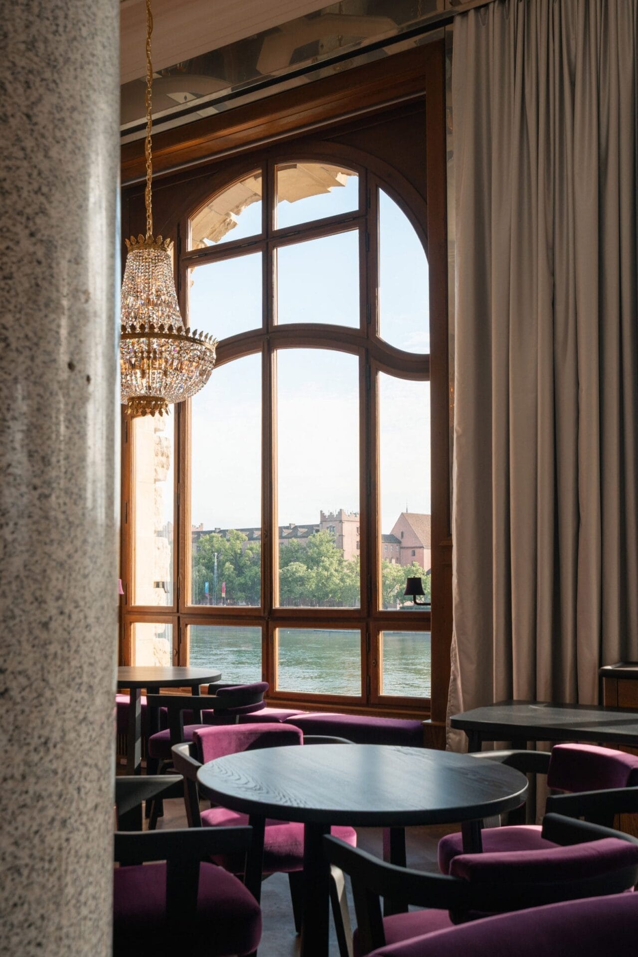 Uitzicht vanuit het restaurant op de Rijn door een groot boogvenster, met paarse stoelen en een kristallen kroonluchter