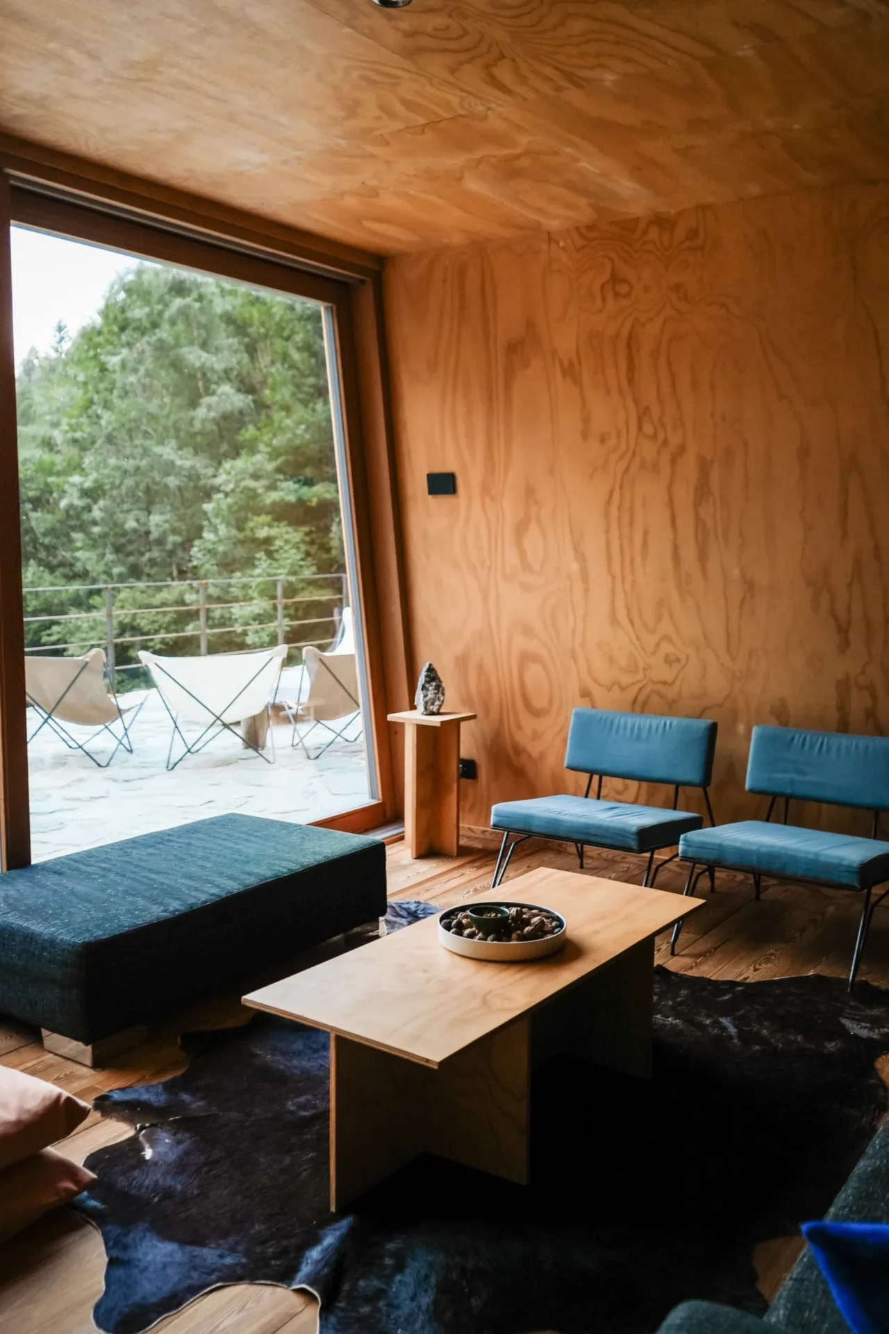 Modern interieur van Rifugio Val di Togno met houten wanden, blauwe stoelen en uitzicht op een terras in de natuur