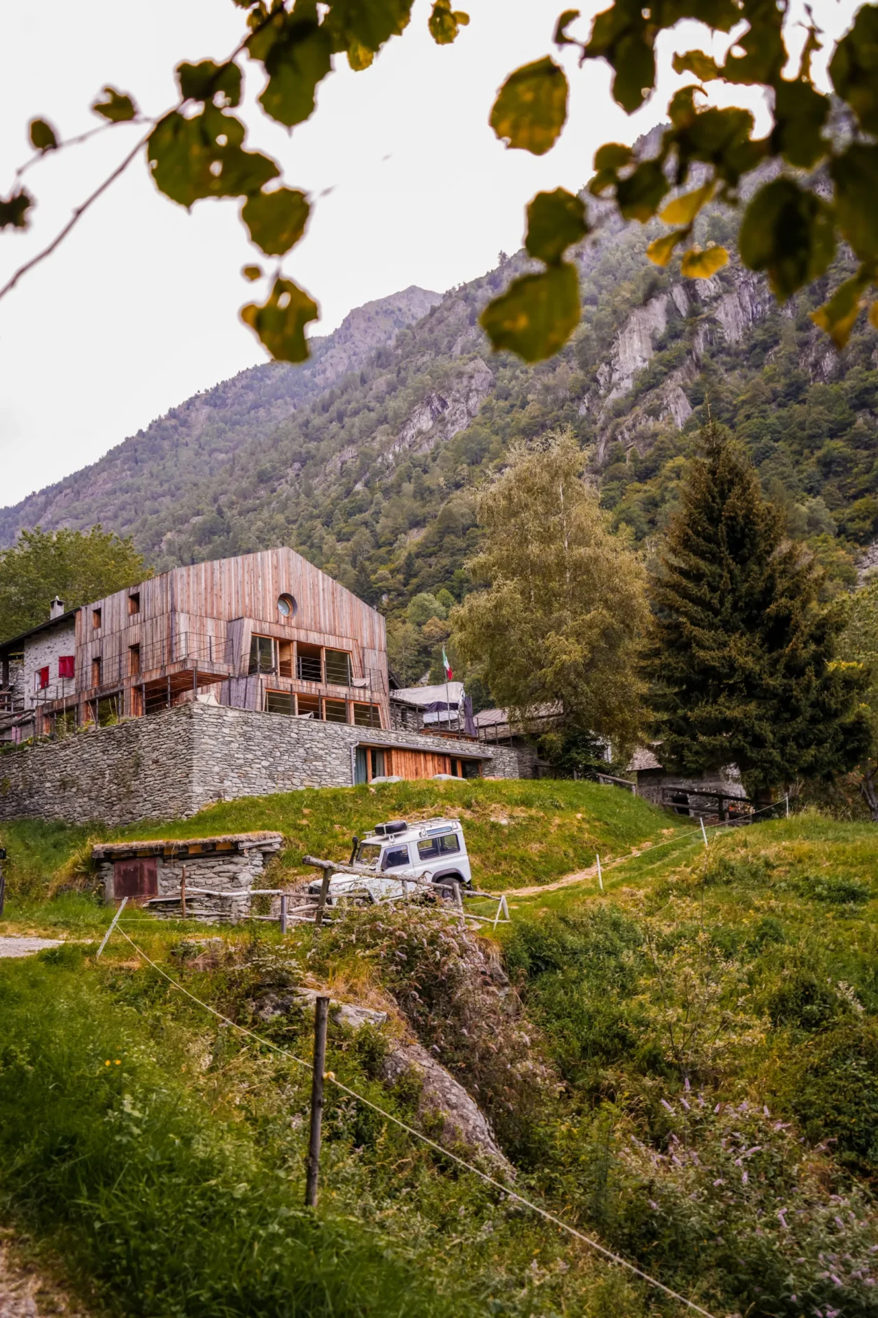 De gerenoveerde houten Rifugio Val di Togno op een stenen fundament in een groene, bergachtige vallei