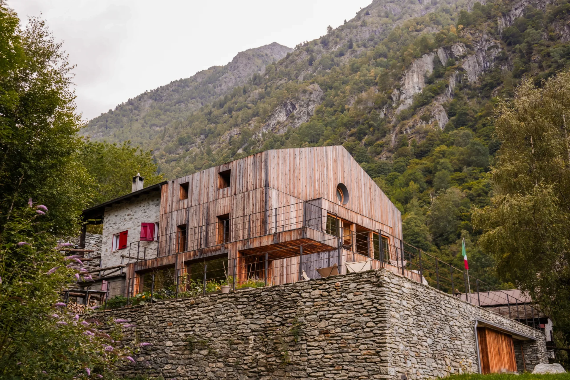 Rifugio Val di Togno: een modern houten gebouw gecombineerd met een stenen structuur, gelegen tegen een beboste bergwand