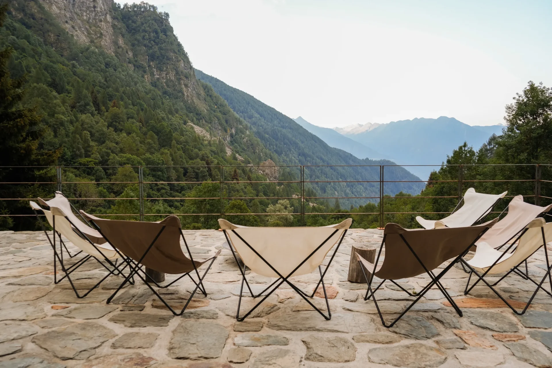 Een stenen terras met vlinderstoelen die uitkijken over een beboste vallei en verre bergtoppen