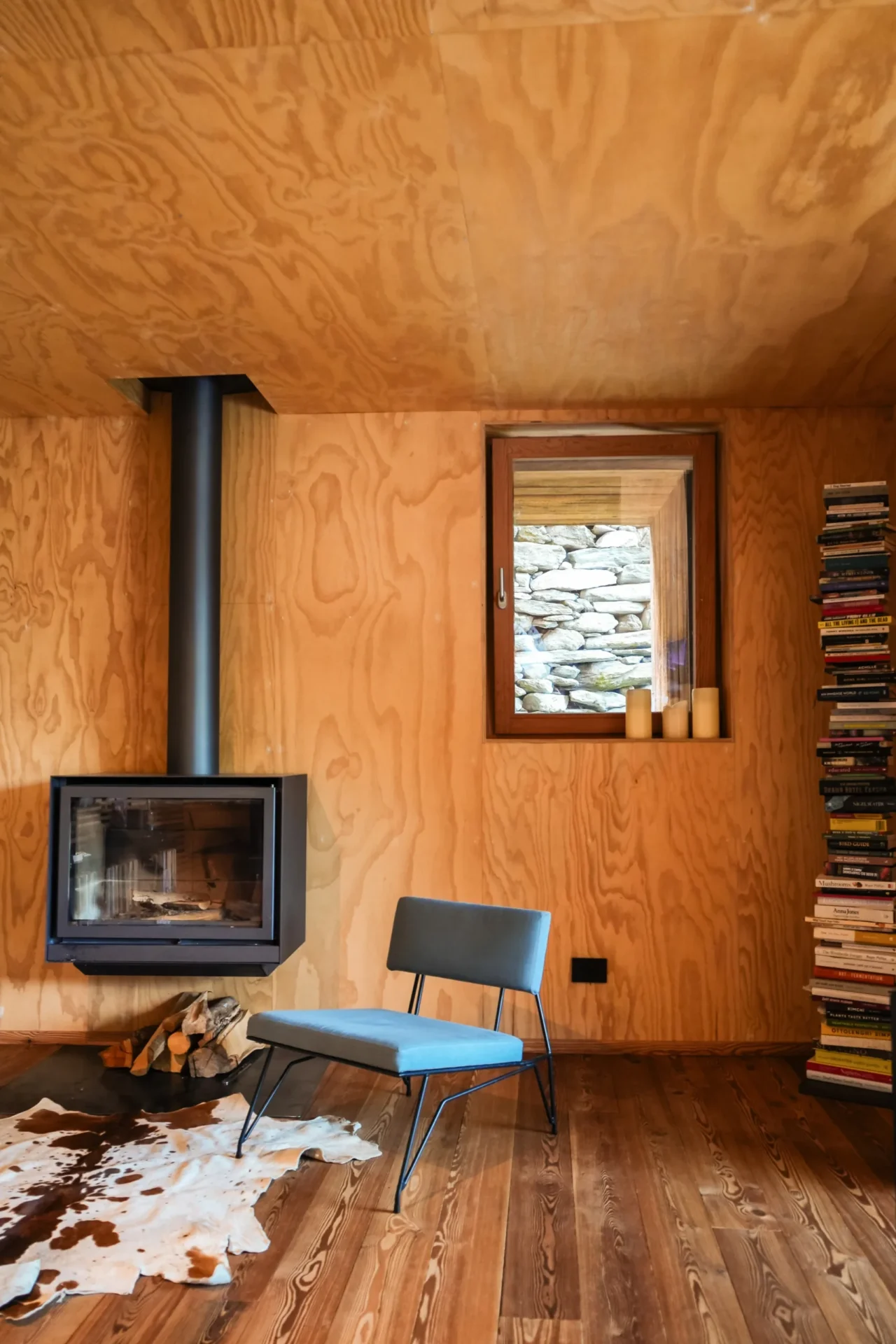 Modern interieur van Rifugio Val di Togno met houten wanden, een designstoel, een zwevende haard en een stapel boeken