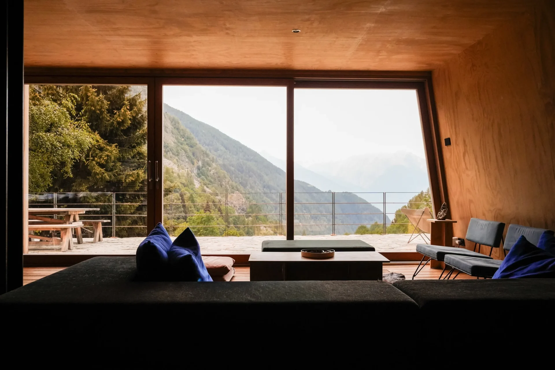 Modern interieur van Rifugio Val di Togno met houten wanden en een groot raam dat uitkijkt over de bergen