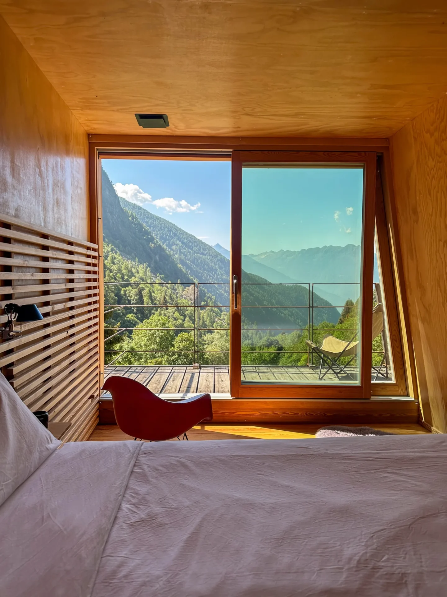 Uitzicht vanuit een moderne houten slaapkamer in Rifugio Val di Togno op de beboste bergen en een zonnig terras