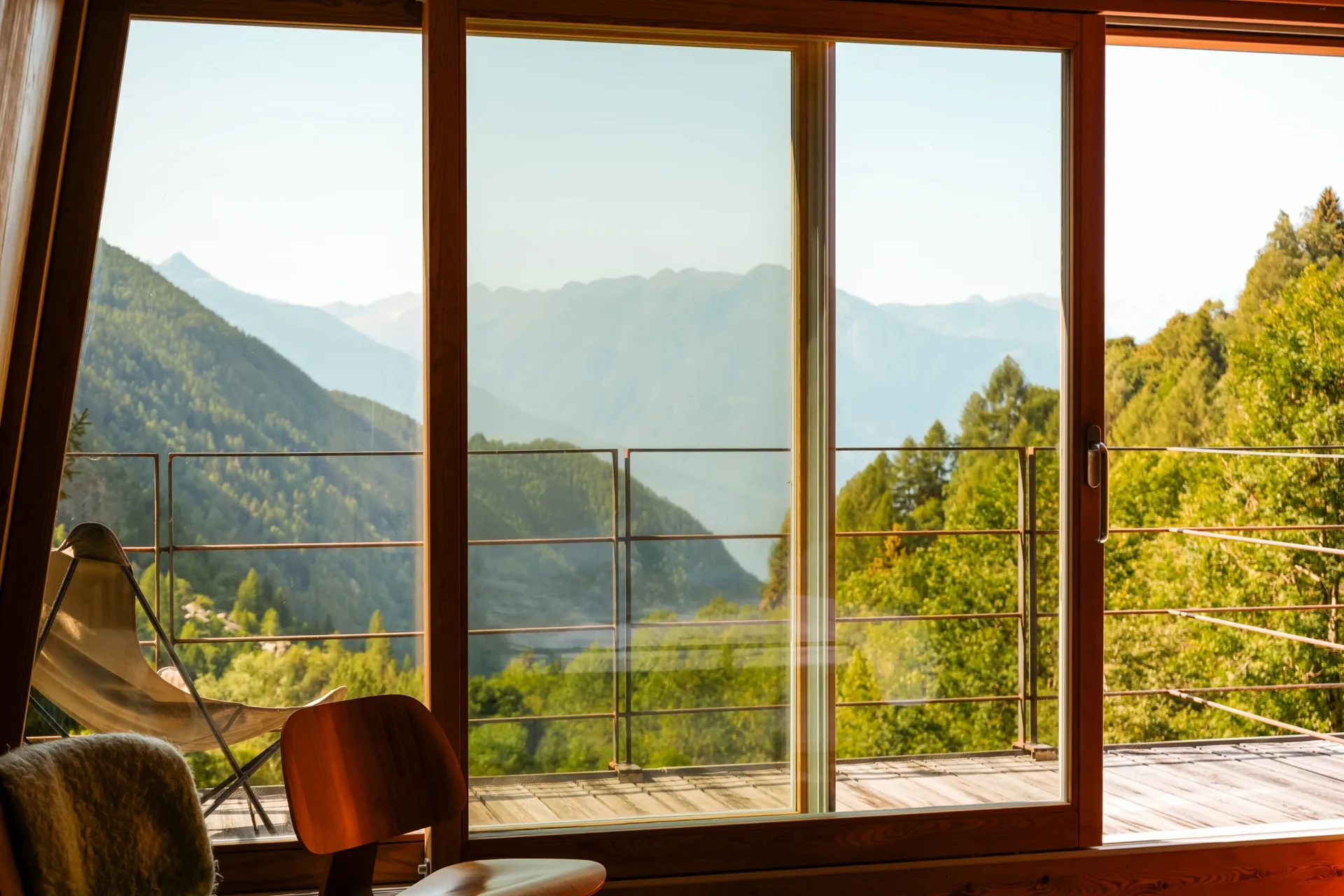 Uitzicht vanuit een kamer in Rifugio Val di Togno op de beboste bergen en een terras met een loungestoel