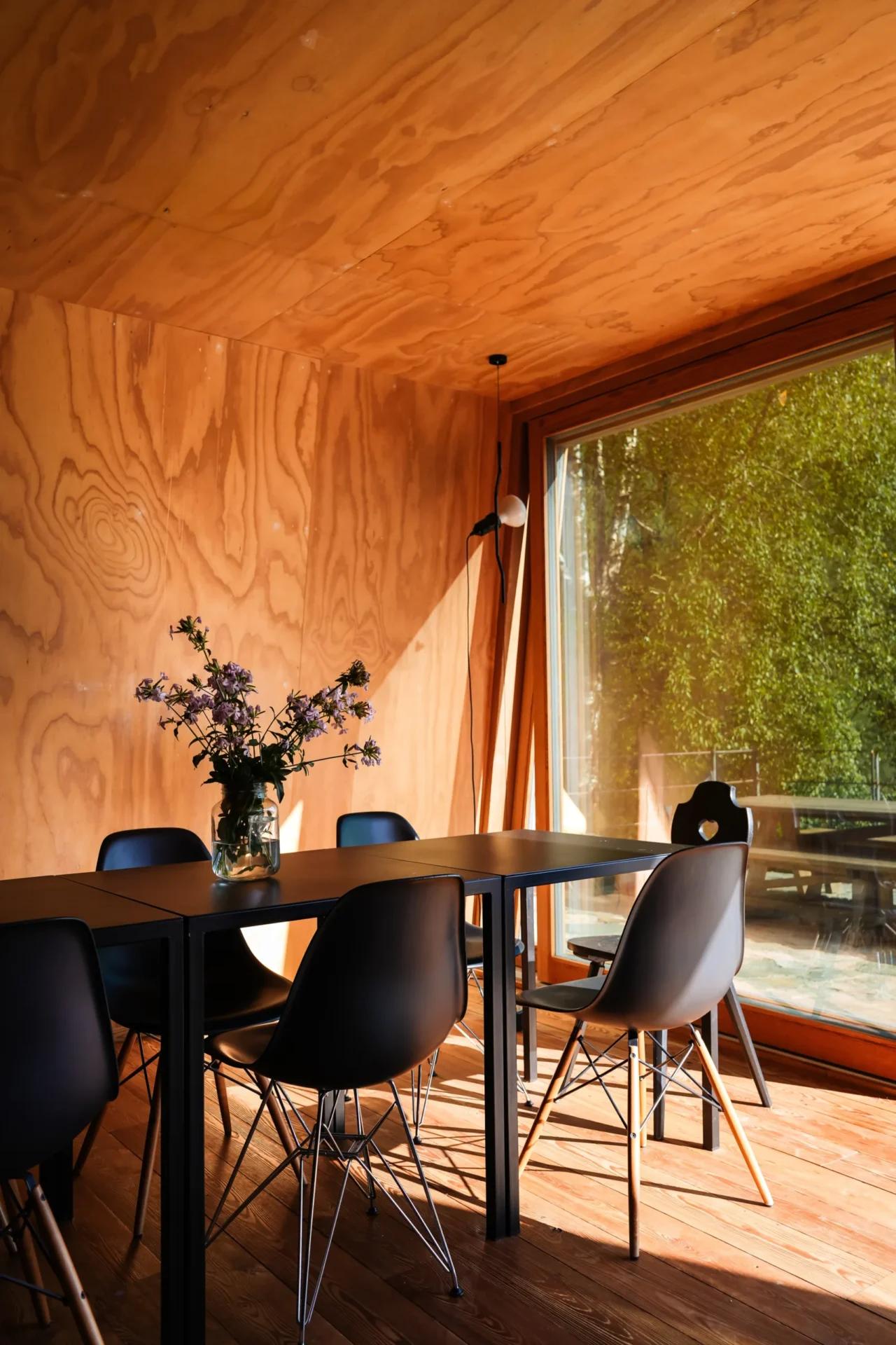 Modern interieur van Rifugio Val di Togno met houten wanden, een zwarte eettafel en uitzicht op de natuur door een groot raam
