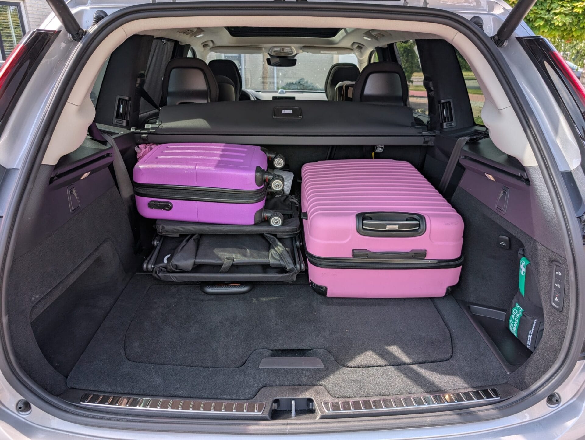 De ruime kofferbak van de Volvo XC90 met twee roze koffers en een bolderkar, waarbij nog veel laadruimte over is