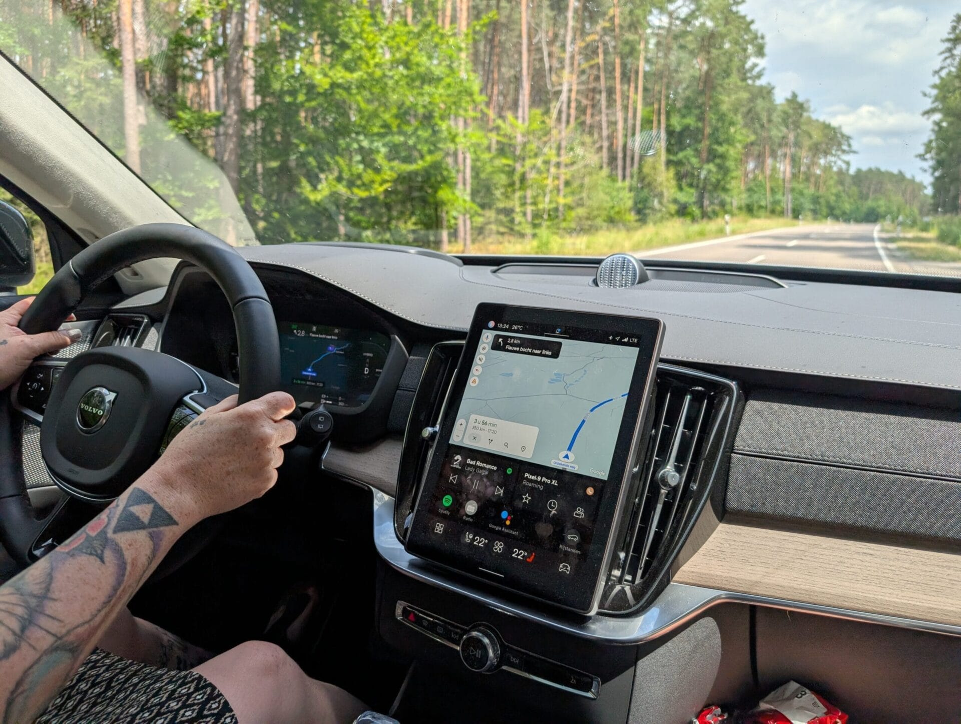 Interieur van de Volvo XC90 met focus op het centrale tablet-scherm waarop Google Maps navigatie en Spotify getoond worden