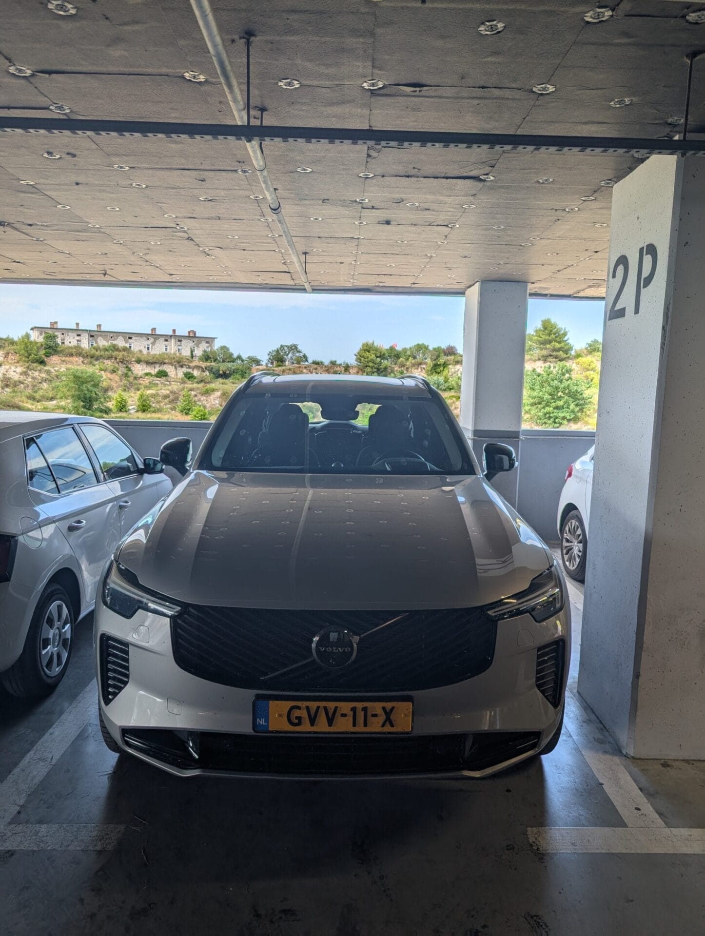 Vooraanzicht van een zilveren Volvo XC90 geparkeerd in een parkeergarage tijdens een vakantiereis