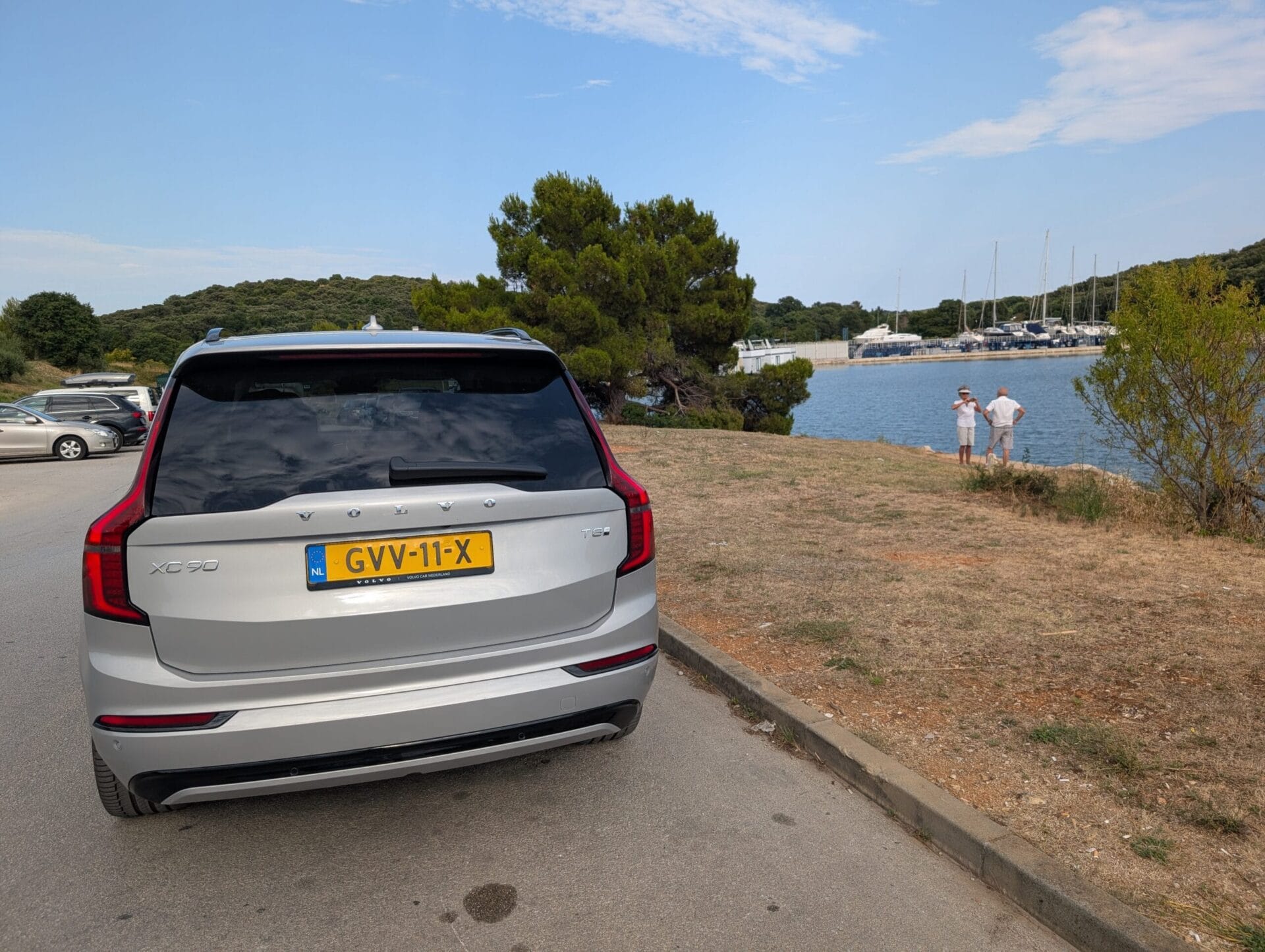 Achteraanzicht van een zilveren Volvo XC90 T8 geparkeerd aan de kust van Kroatië met een jachthaven op de achtergrond