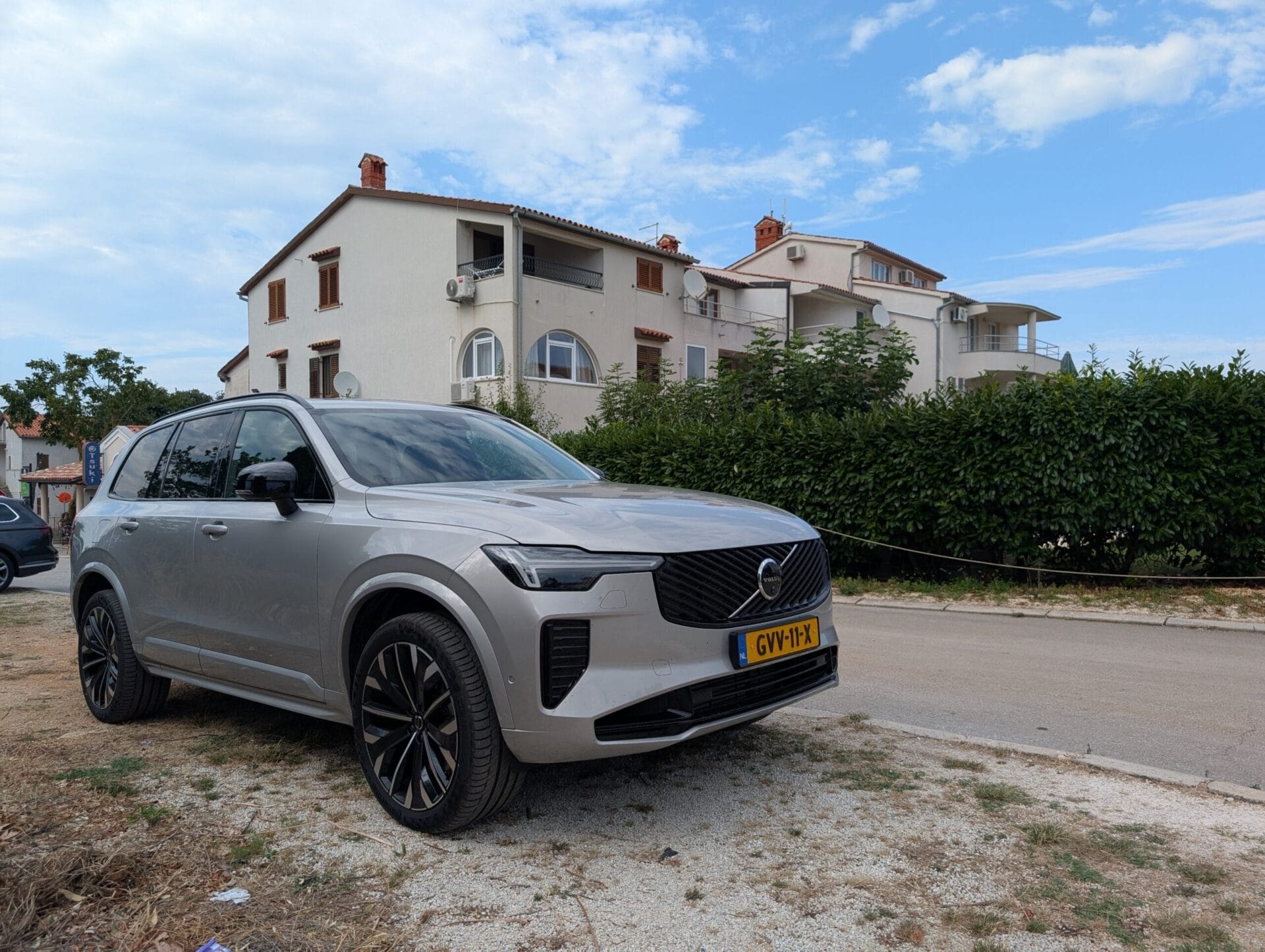 Zilveren Volvo XC90 T8 geparkeerd voor een wit appartementencomplex in Kroatië onder een blauwe lucht