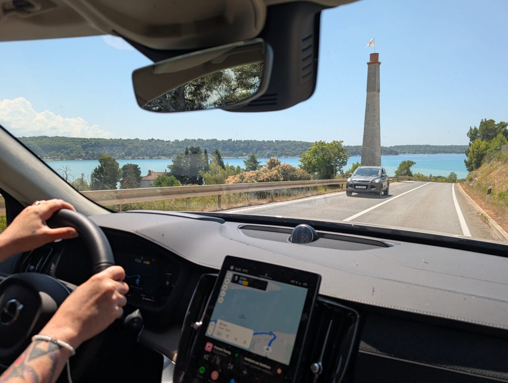 Uitzicht vanuit de Volvo XC90 op een kustweg in Kroatië met een stenen toren en blauw water op de achtergrond