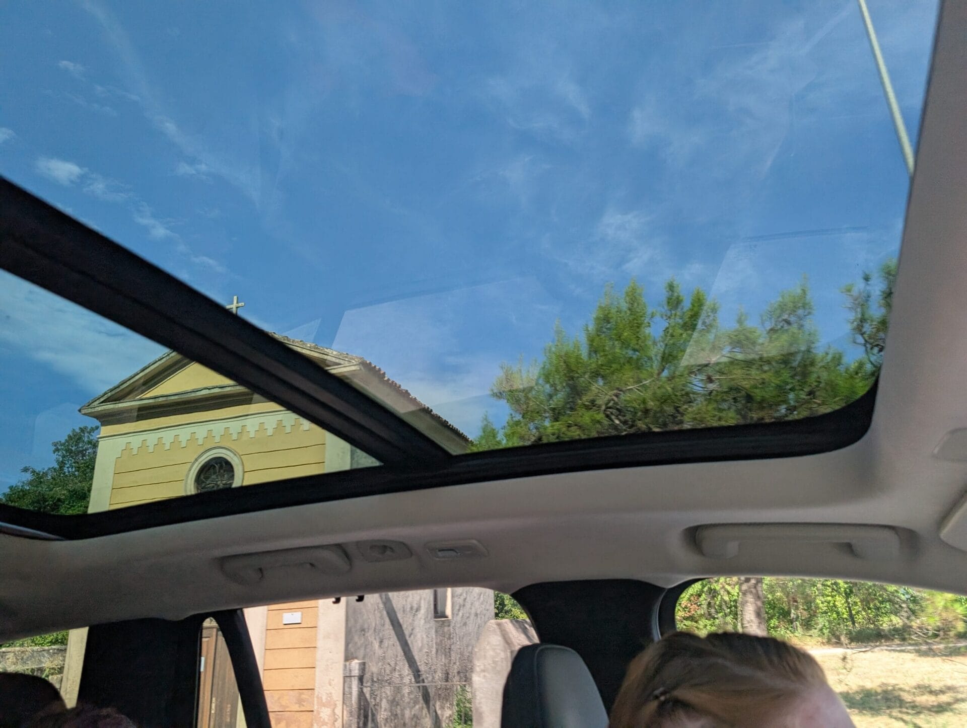 Zicht door het glazen panoramadak van de Volvo XC90 op een blauwe lucht en een geel kerkje