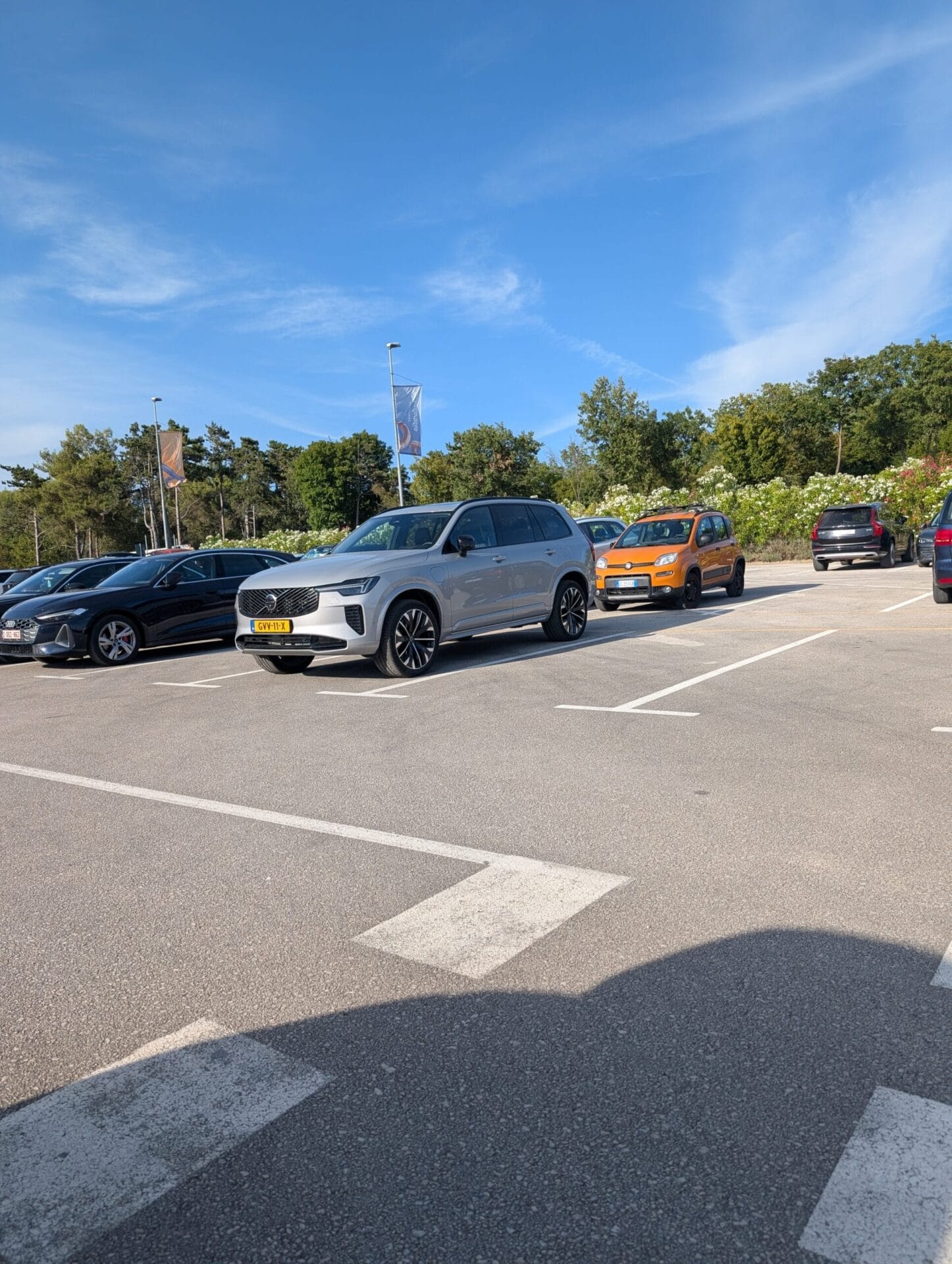Zijaanzicht van een zilveren Volvo XC90 geparkeerd op een zonnige parkeerplaats tijdens een vakantiereis