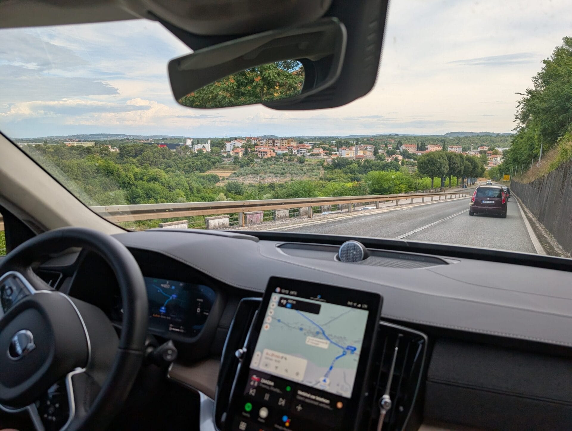 Uitzicht vanuit de cockpit van de Volvo XC90 op een heuvelachtig landschap met een dorpje in de verte