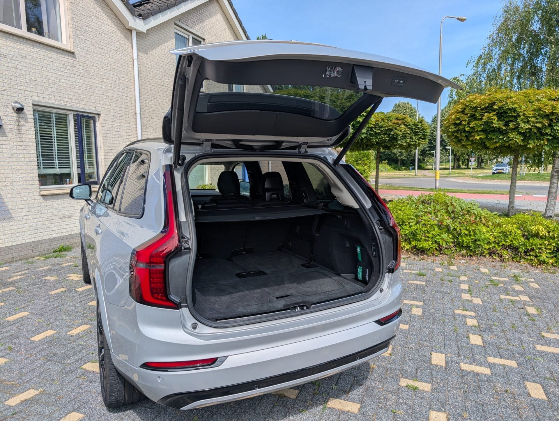 De geopende, ruime kofferbak van een zilveren Volvo XC90 geparkeerd op een oprit
