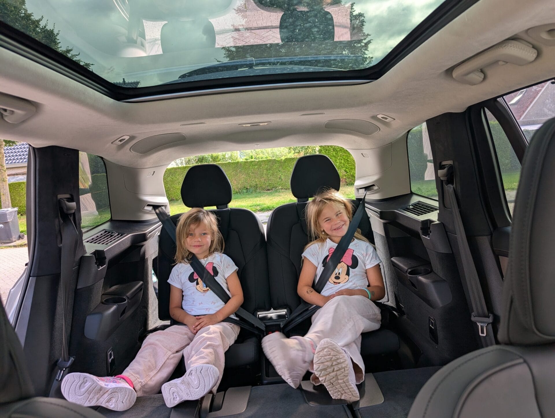 Twee jonge meisjes zitten lachend op de derde zitrij van een Volvo XC90 met een groot glazen panoramadak