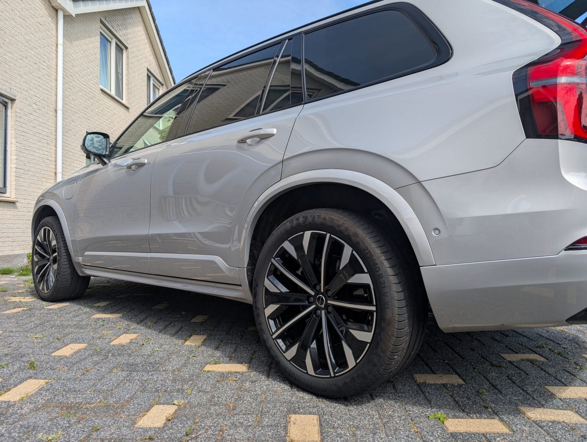 Zijaanzicht van een zilverkleurige Volvo XC90 T8 geparkeerd op een oprit naast een woning