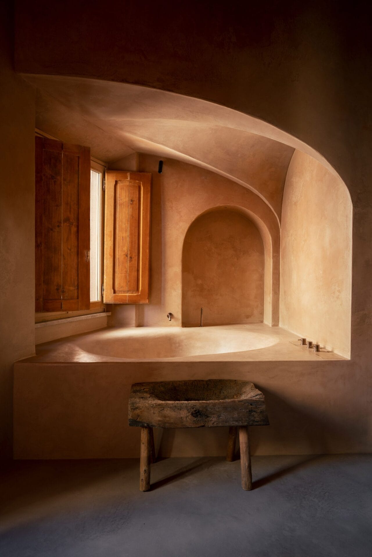 Een minimalistische badkamer in wabi-sabi-stijl met een rond ingebouwd bad, muren van kalkverf en een houten bankje