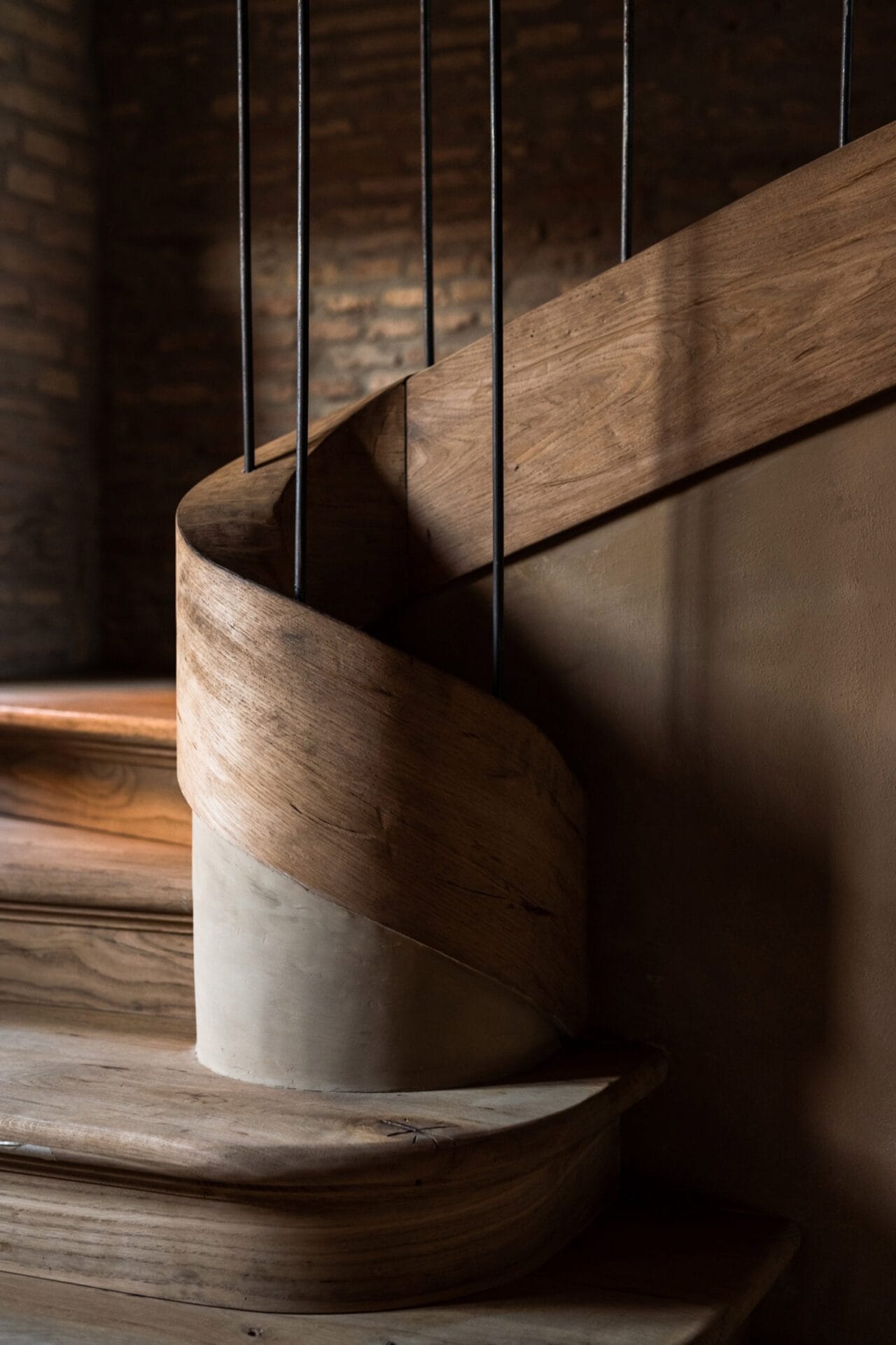 Detail van een robuuste houten wenteltrap met metalen spijlen tegen een achtergrond van een bakstenen muur