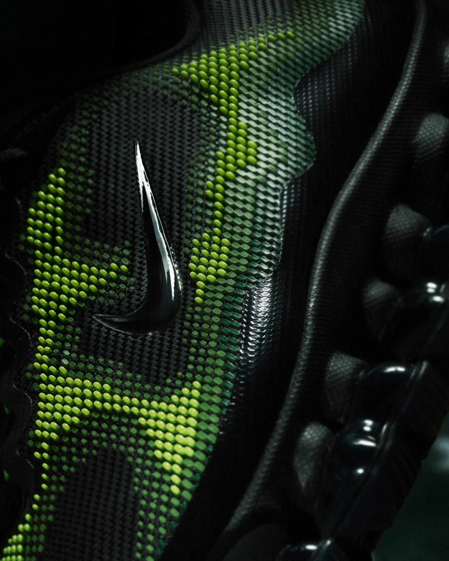 Detailopname van de Nike Air Liquid Max met een chromen Swoosh op een zwart-groen bovenwerk met 3D-noppenstructuur