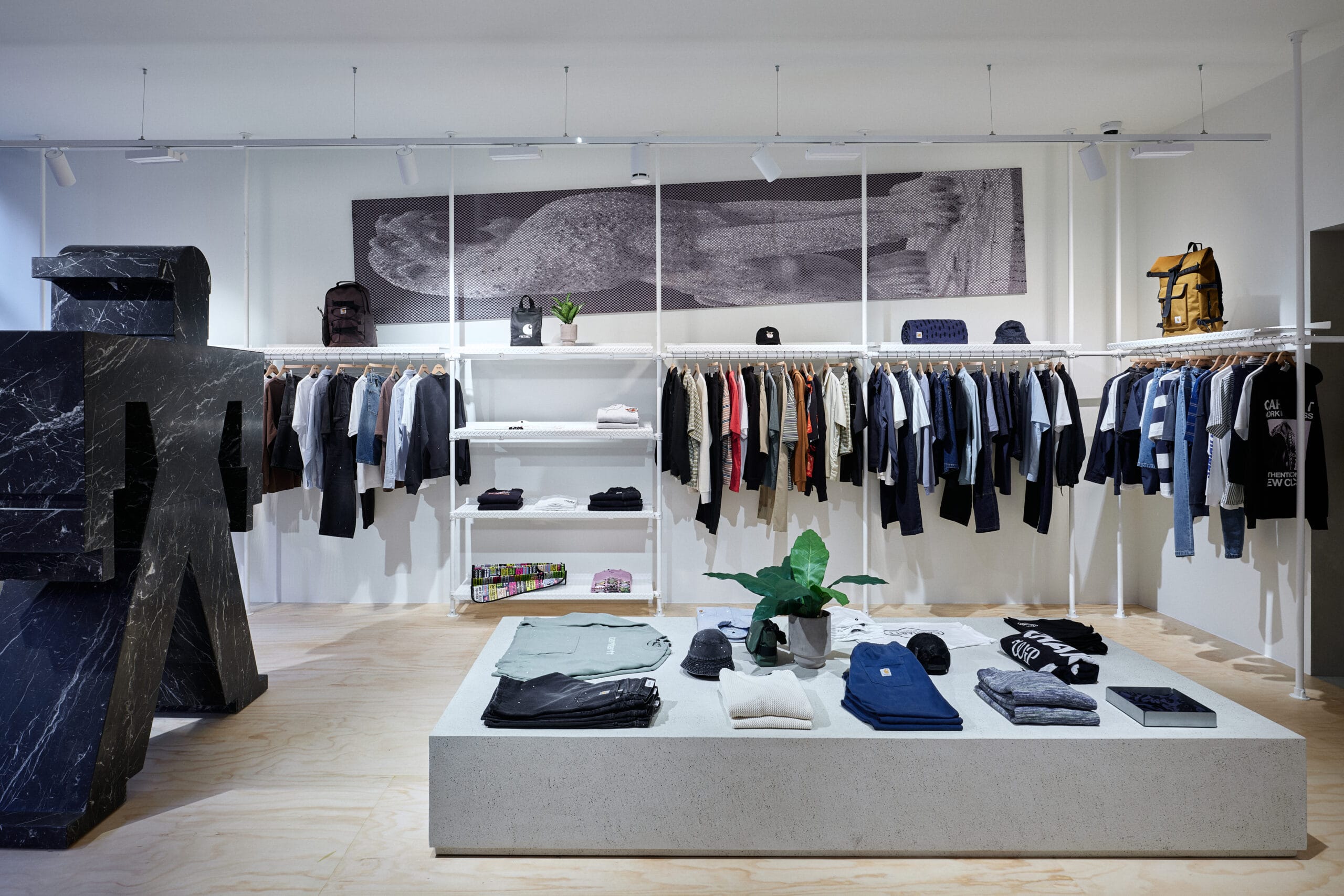 Interieur van een moderne kledingwinkel met kledingrekken, een centrale displaytafel en een groot zwart marmeren sculptuur