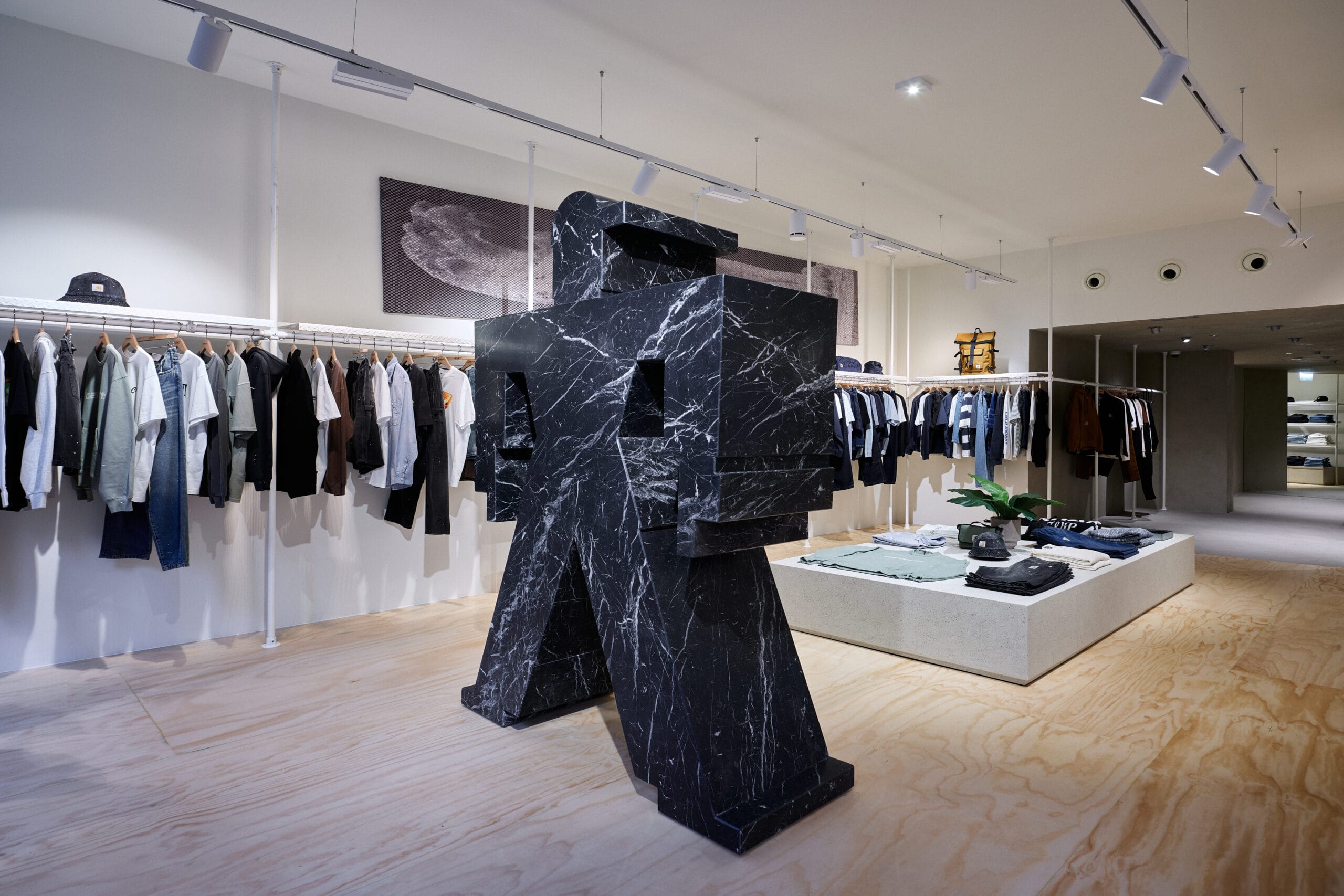 Interieur van een kledingwinkel met een groot abstract zwart marmeren beeld in het midden en kledingrekken aan de wanden