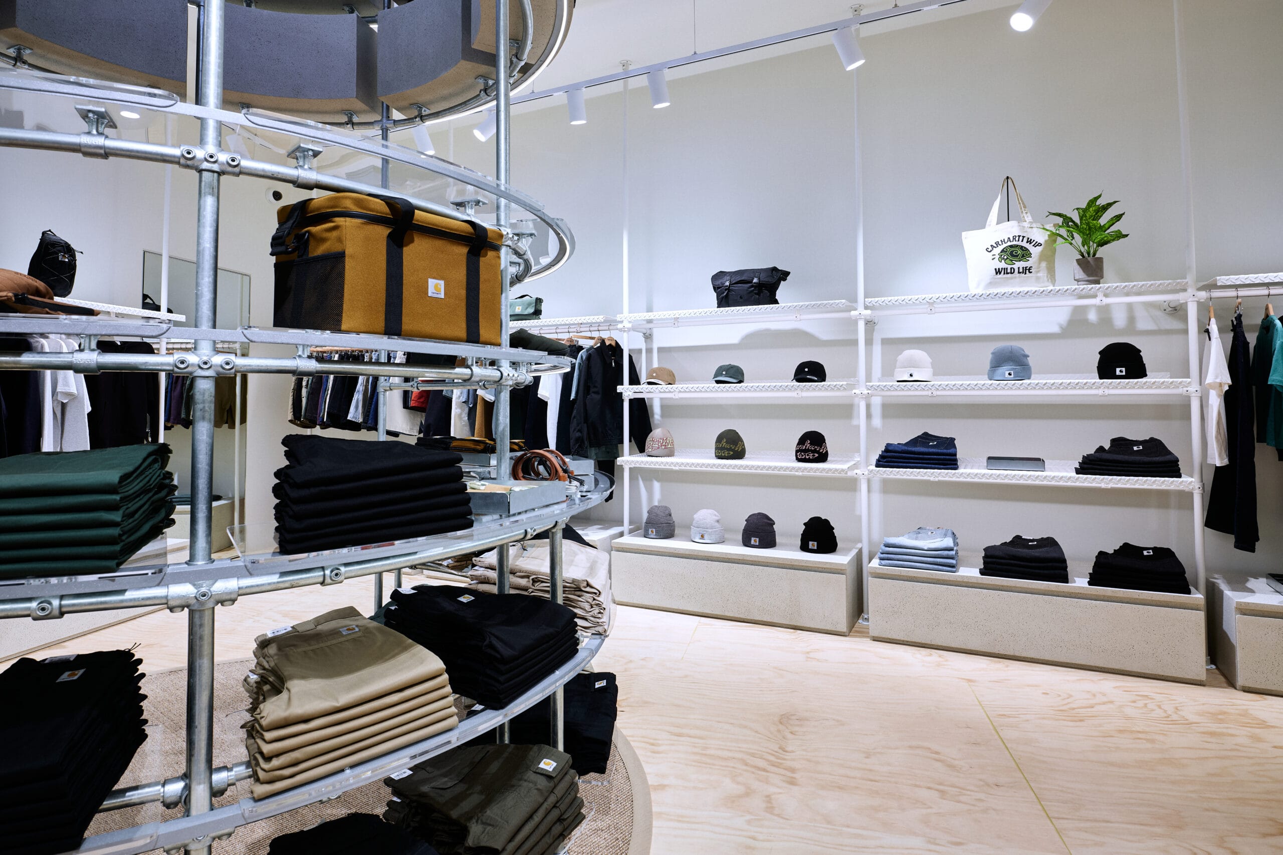 Interieur van een moderne kledingwinkel met industriële stellingen, gevuld met gevouwen broeken, tassen en mutsen