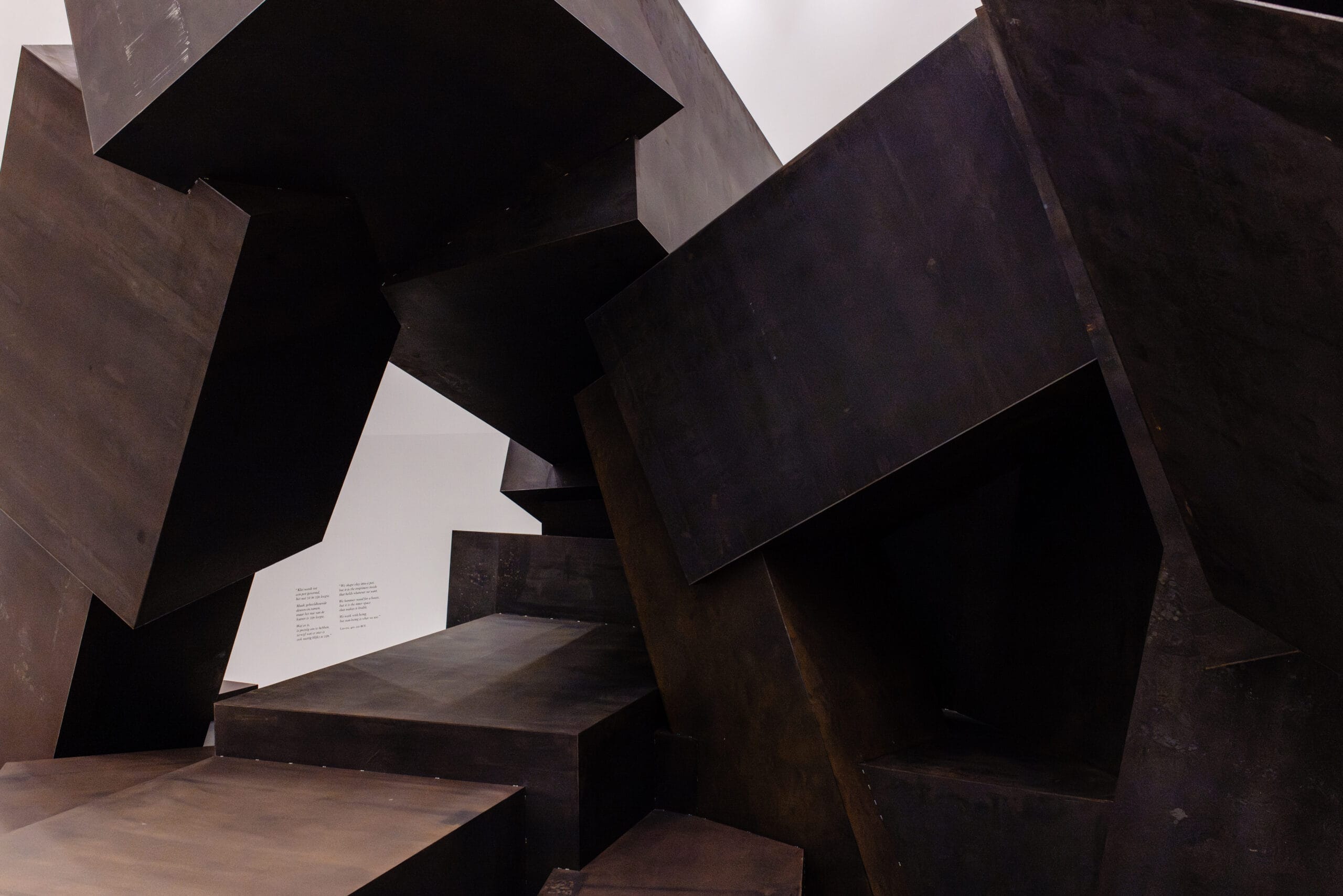 Abstracte sculptuur van grote, opgestapelde donkere metalen blokken in een museumruimte