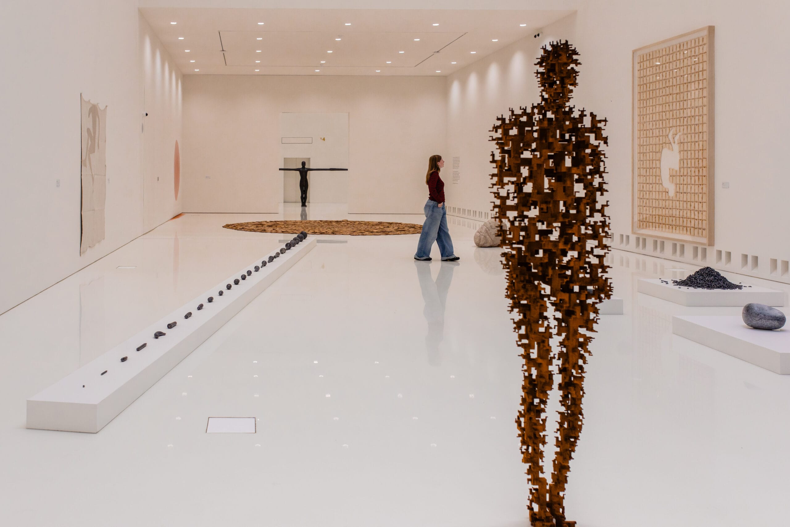 Een bezoeker in een witte museumzaal met diverse moderne sculpturen en kunstwerken van Antony Gormley
