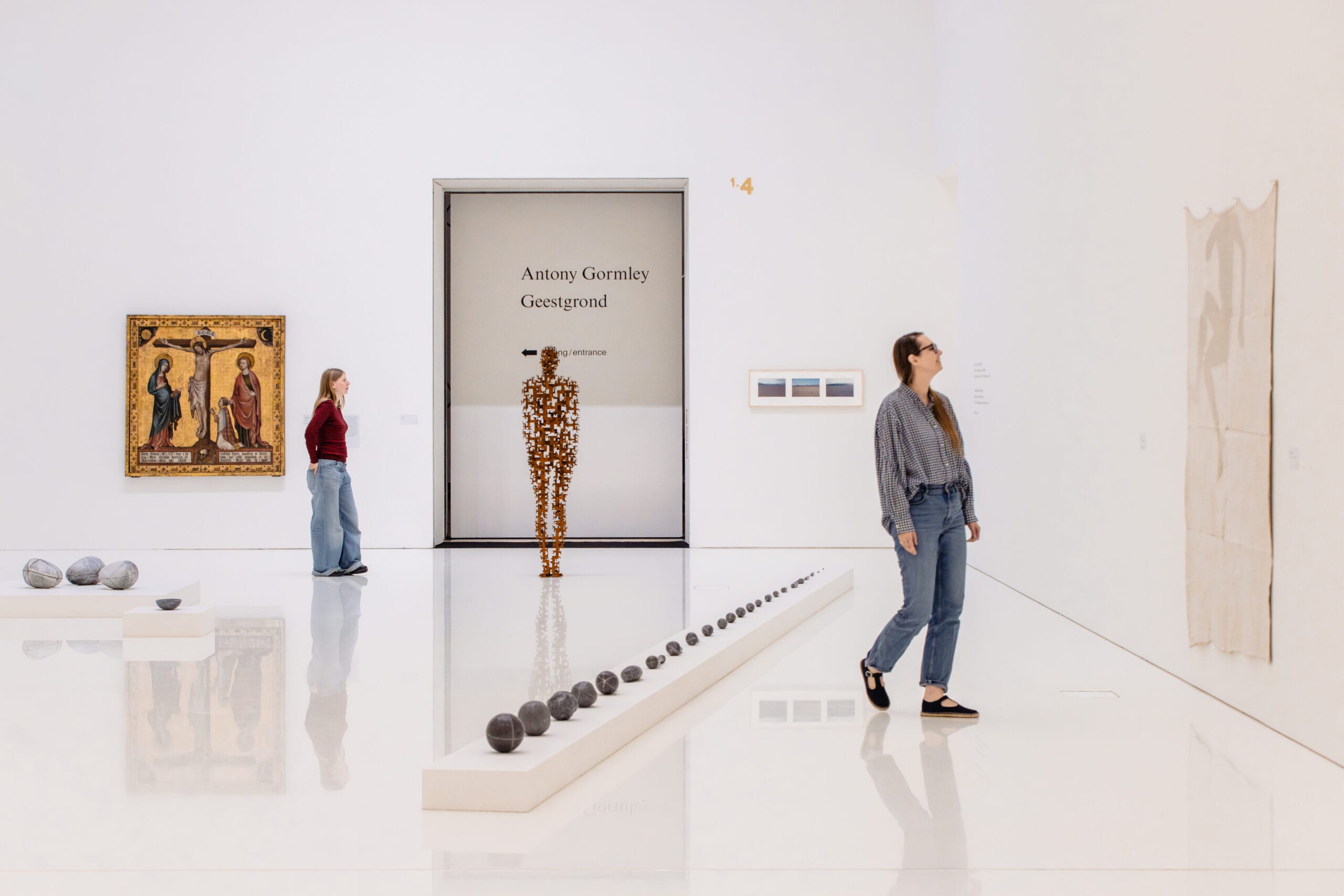 Bezoekers in een lichte museumzaal met diverse kunstwerken, waaronder de sculptuur Geestgrond van Antony Gormley