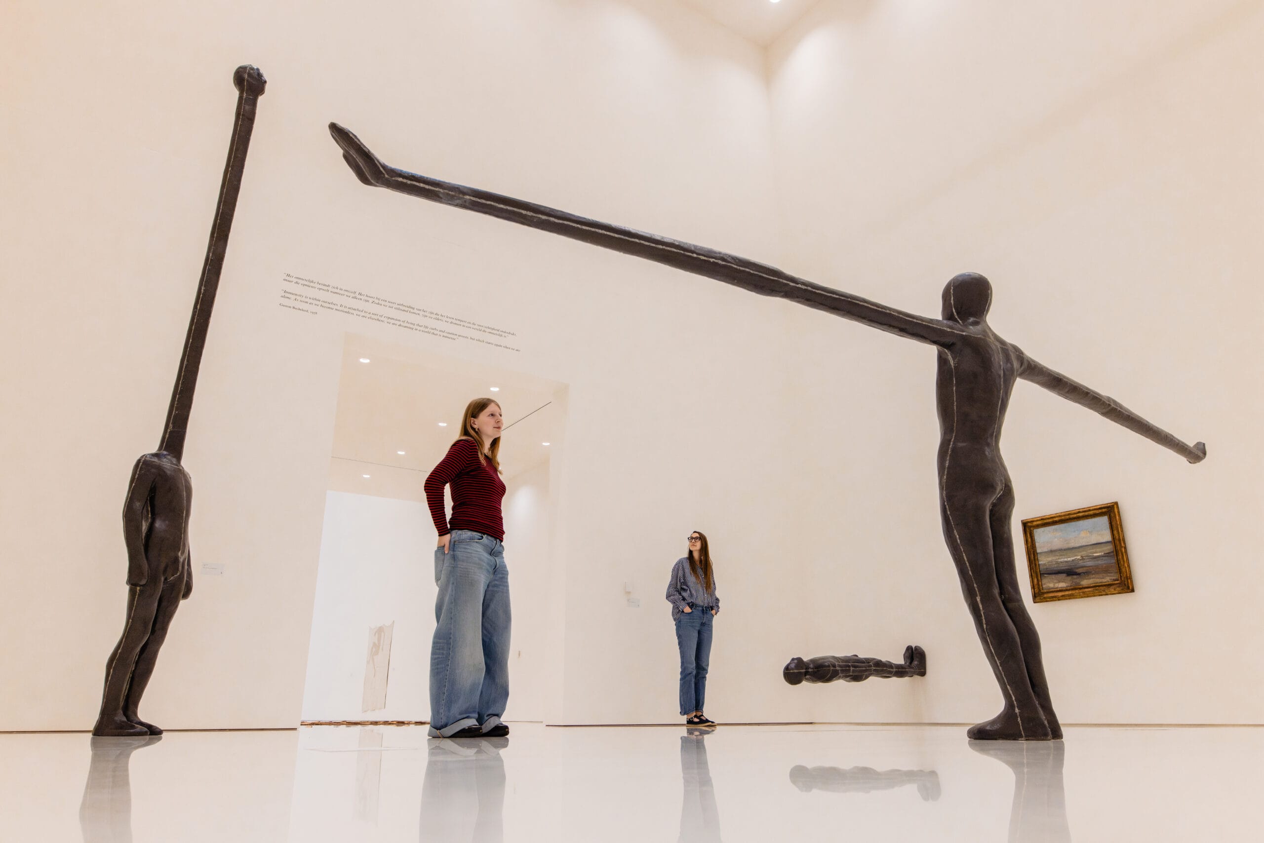 Bezoekers in een museumzaal met abstracte, langgerekte menselijke sculpturen van Antony Gormley