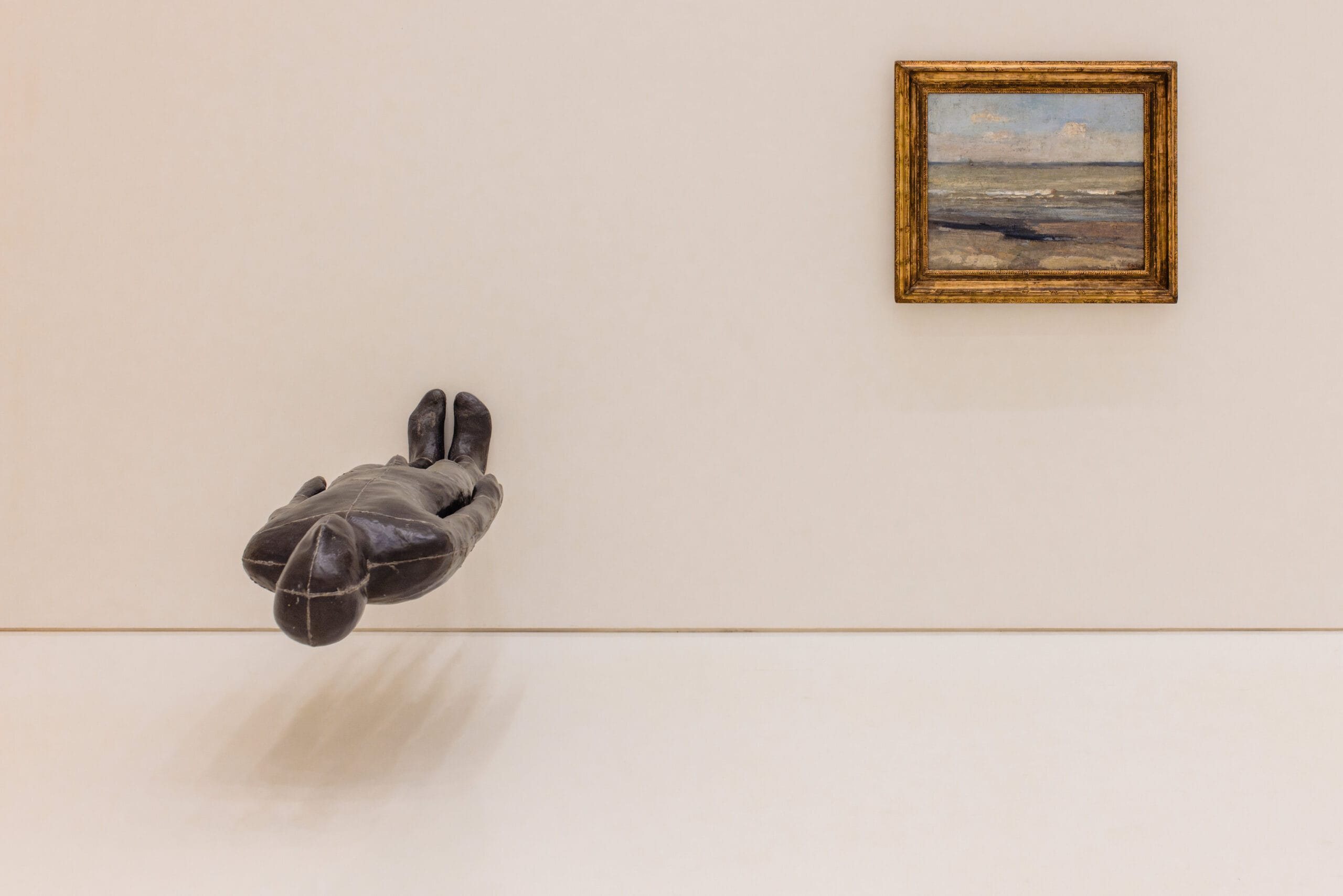 Een donker sculptuur van een zwevende menselijke figuur naast een schilderij van een zeegezicht in een museum