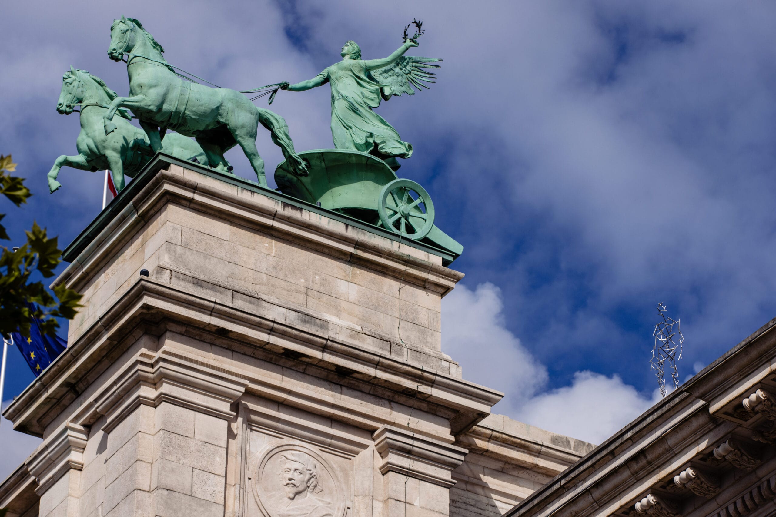 Het bronzen beeld van de Quadriga bovenop de Triomfboog in het Jubelpark te Brussel tegen een blauwe lucht met wolken