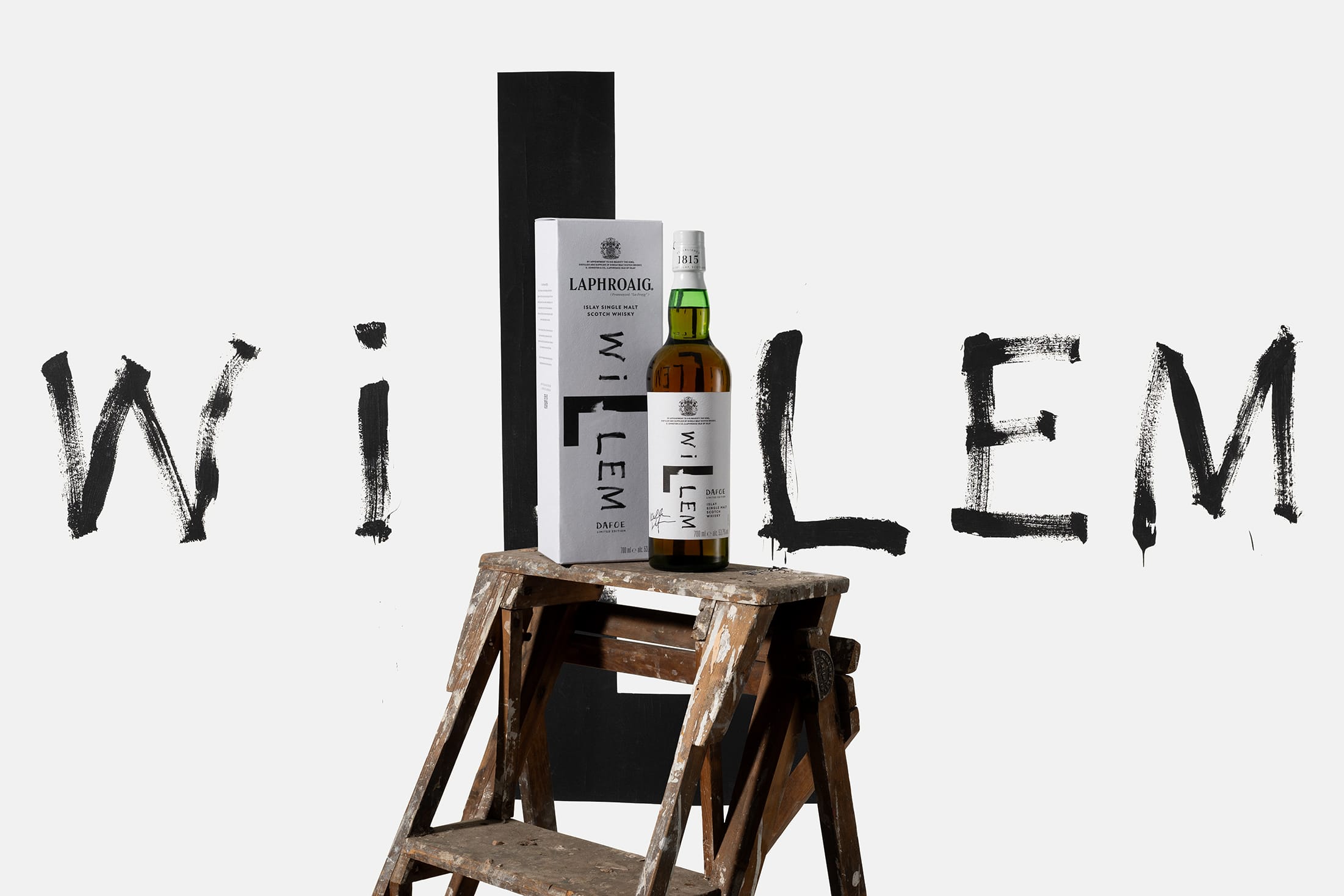 Een fles en verpakking van Laphroaig Willem Dafoe Limited Edition op een houten ladder tegen een wit-zwarte achtergrond