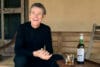 Willem Dafoe lachend op een houten bank naast een fles Willem Dafoe Islay Single Malt Scotch Whisky