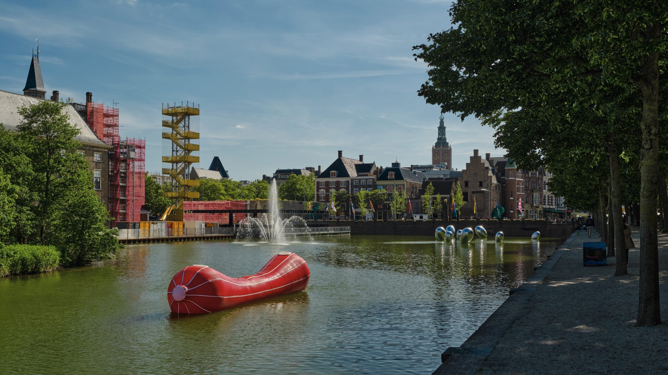 Zicht op de Hofvijver in Den Haag met een opblaasbaar kunstwerk, fonteinen en de skyline van het Binnenhof