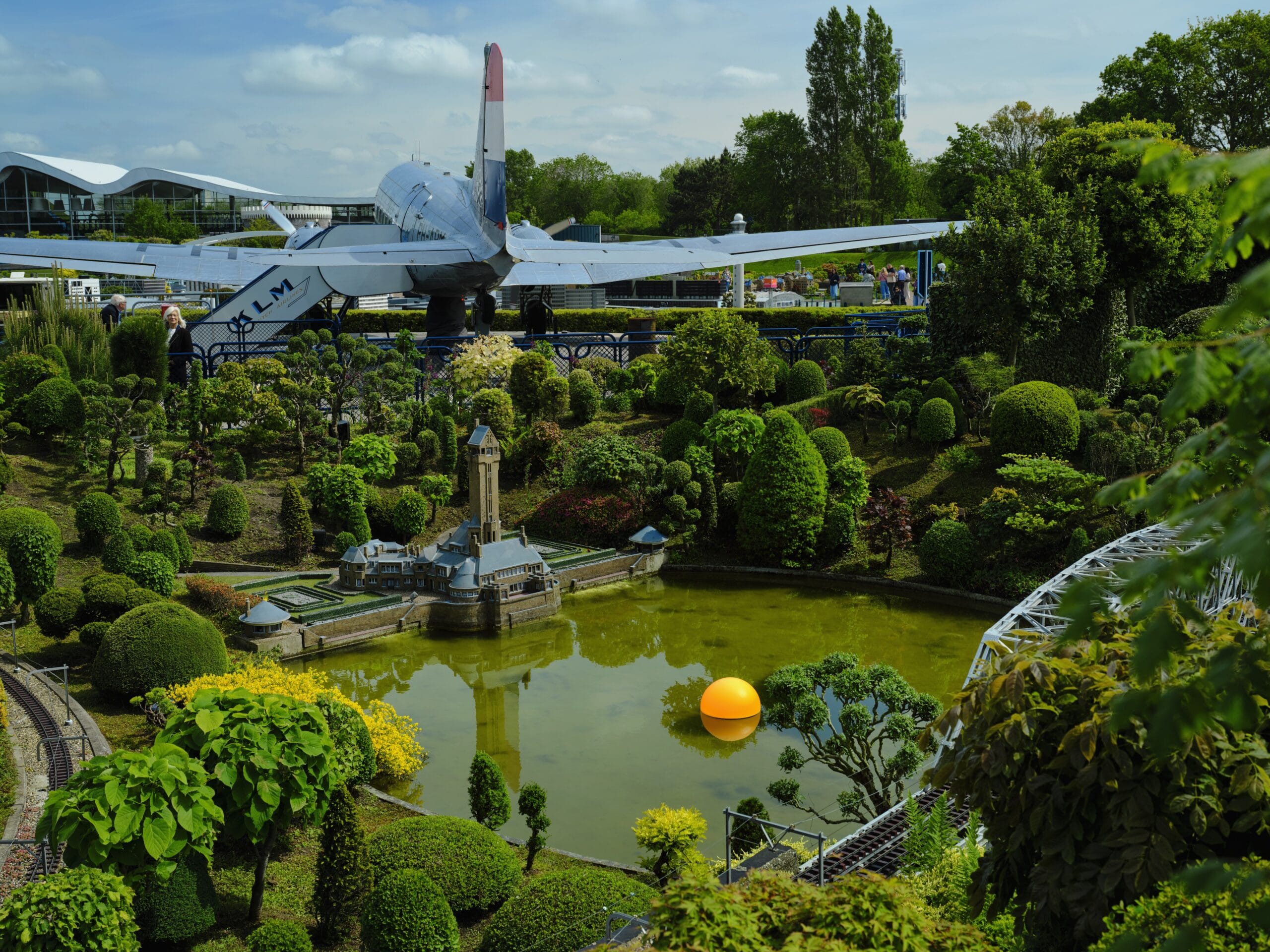 Miniatuurpark Madurodam met een model van een kasteel aan een vijver en een groot KLM-vliegtuig op de achtergrond