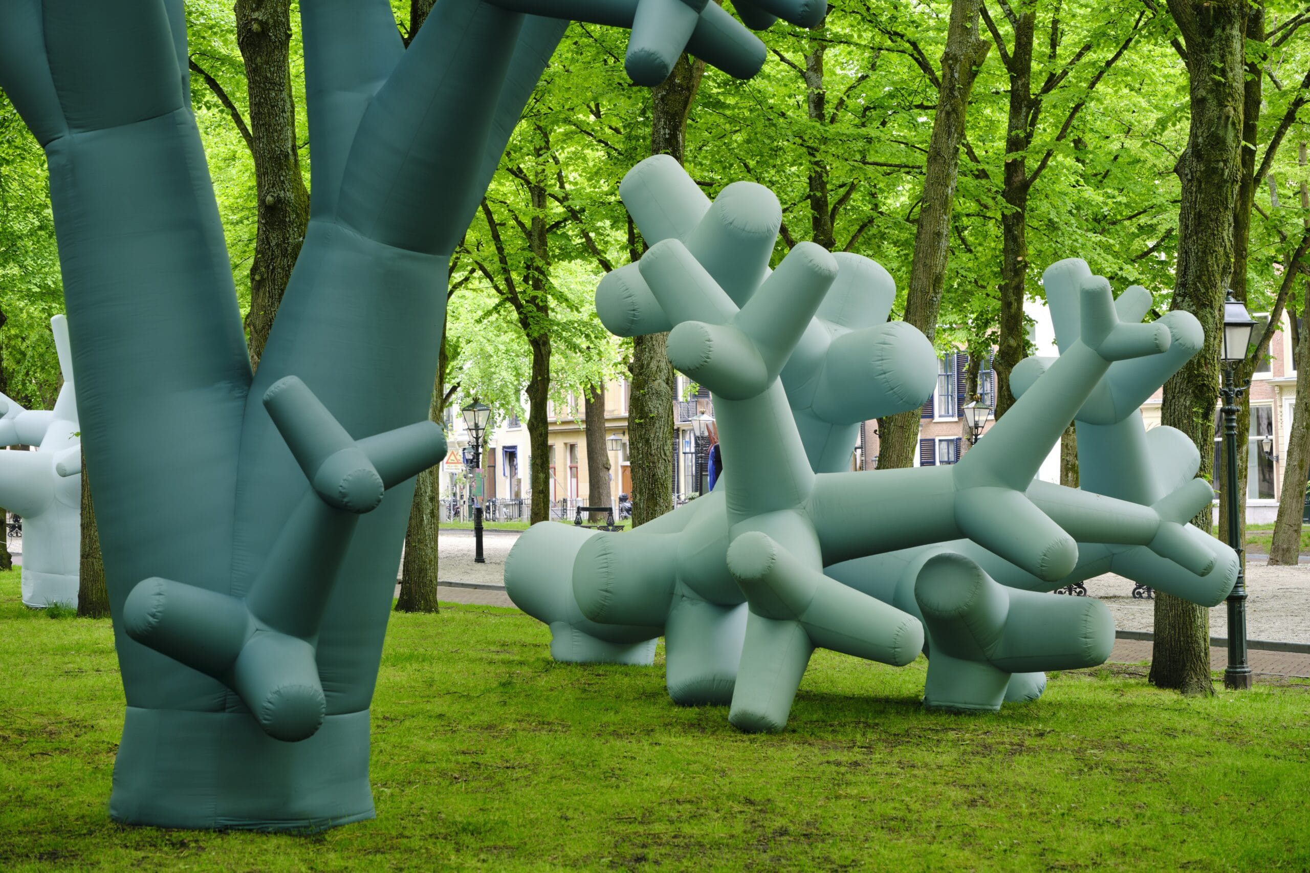 Grote, lichtblauwe opblaasbare sculpturen in de vorm van abstracte bomen in een park met echte groene bomen
