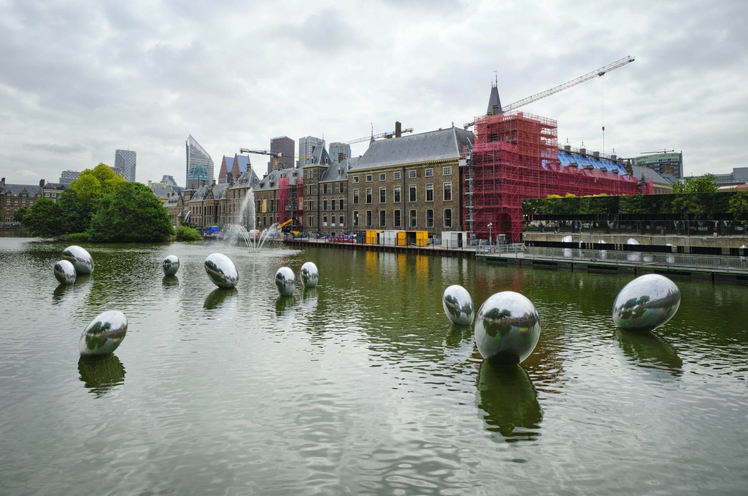Zilveren eivormige kunstwerken drijvend in de Hofvijver met het Binnenhof in de steigers op de achtergrond