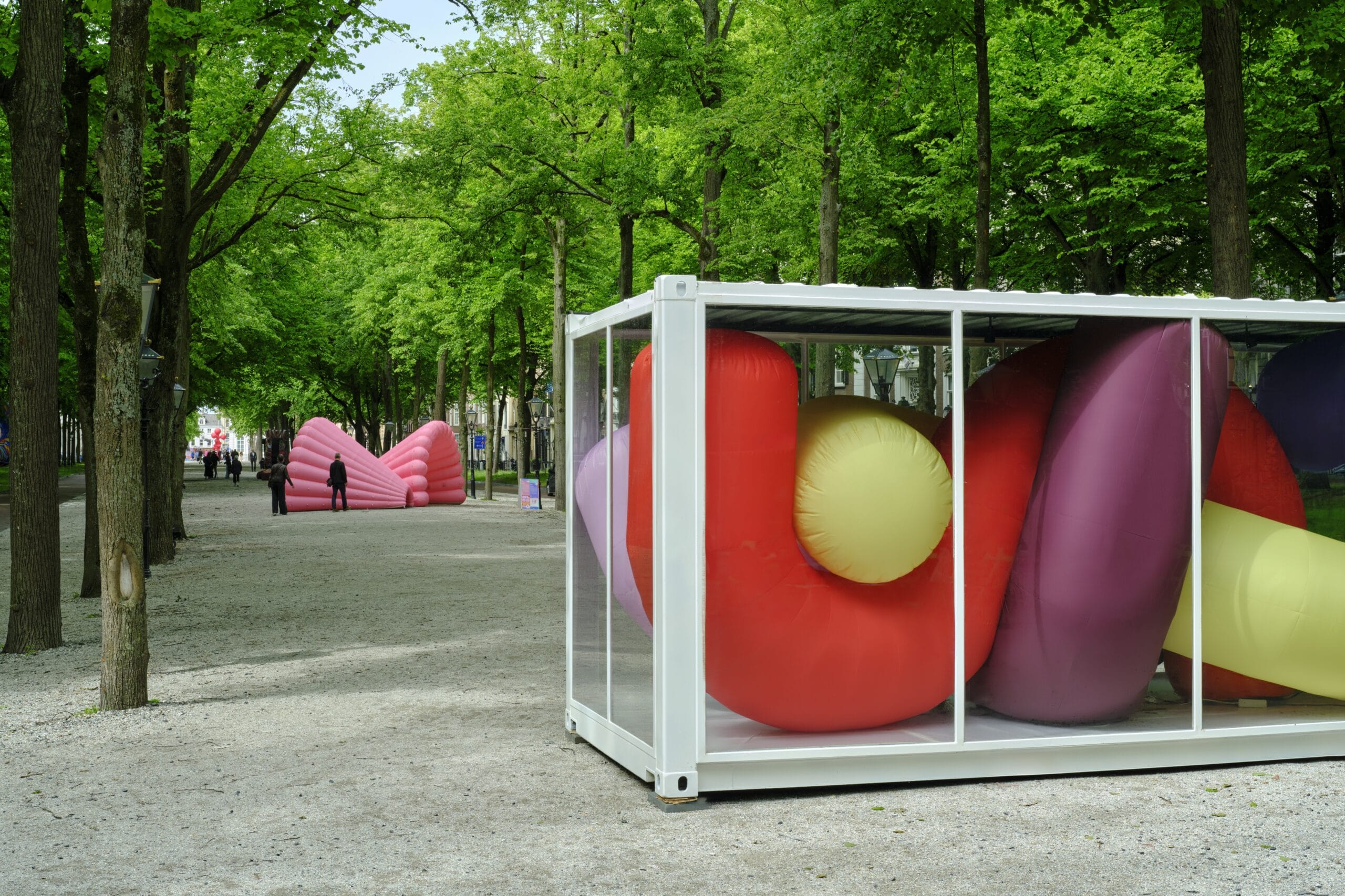 Kleurrijke opblaasbare vormen in een glazen container op een bomenlaan tijdens de kunsttentoonstelling Voorhout Monumentaal